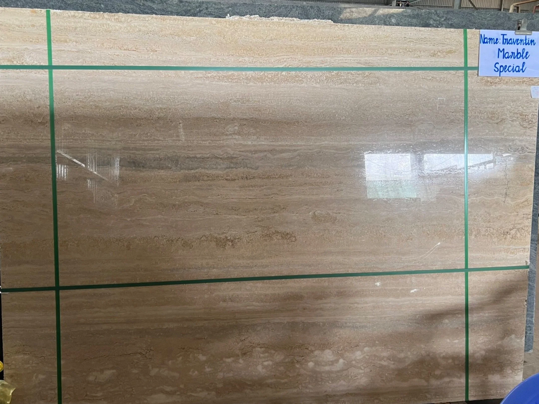 Slab of Travertine Marble with a glossy finish and subtle brown veining, labeled 'Travertin Marble Special' in a warehouse setting.