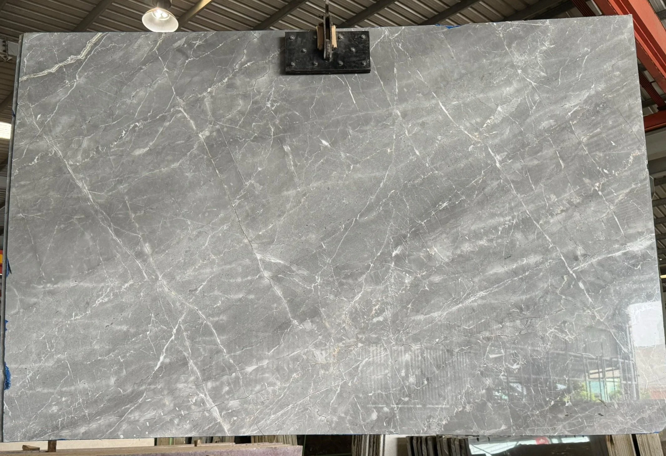 Large slab of grey marble with white veining displayed in a showroom with a metal roof.