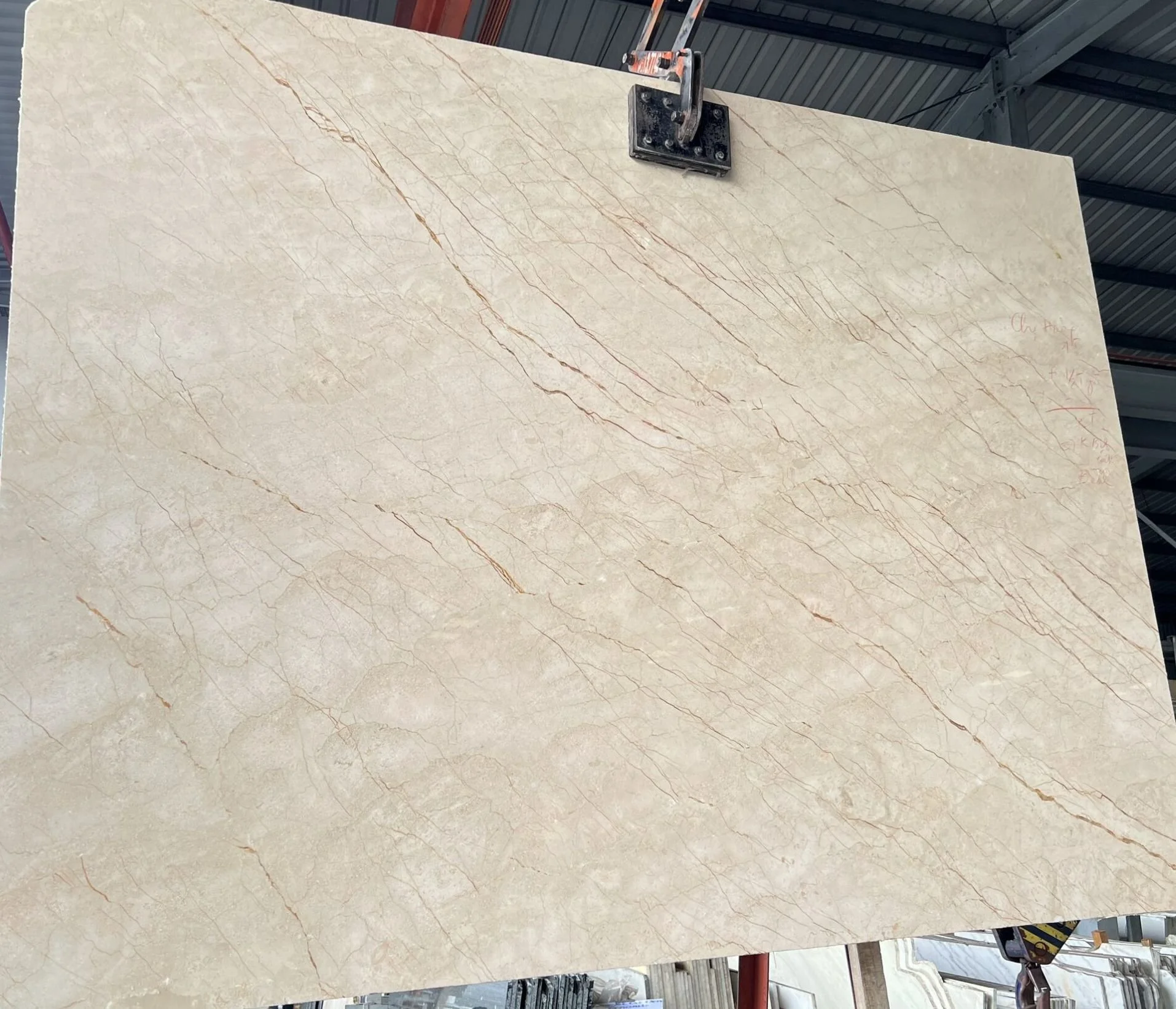 Large beige marble slab with brown veining in warehouse setting.