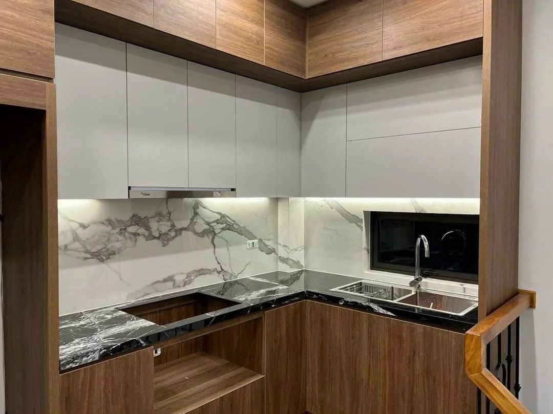 Modern kitchen with wooden cabinets, white marble backsplash, black countertops, and stainless steel sink.
