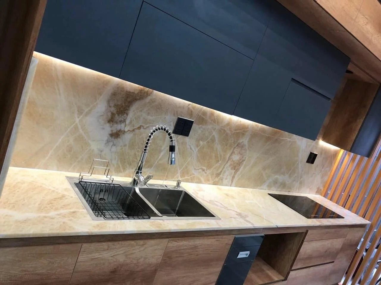 Modern kitchen with marble countertops, dual sinks, marble backsplash, and wooden cabinets.