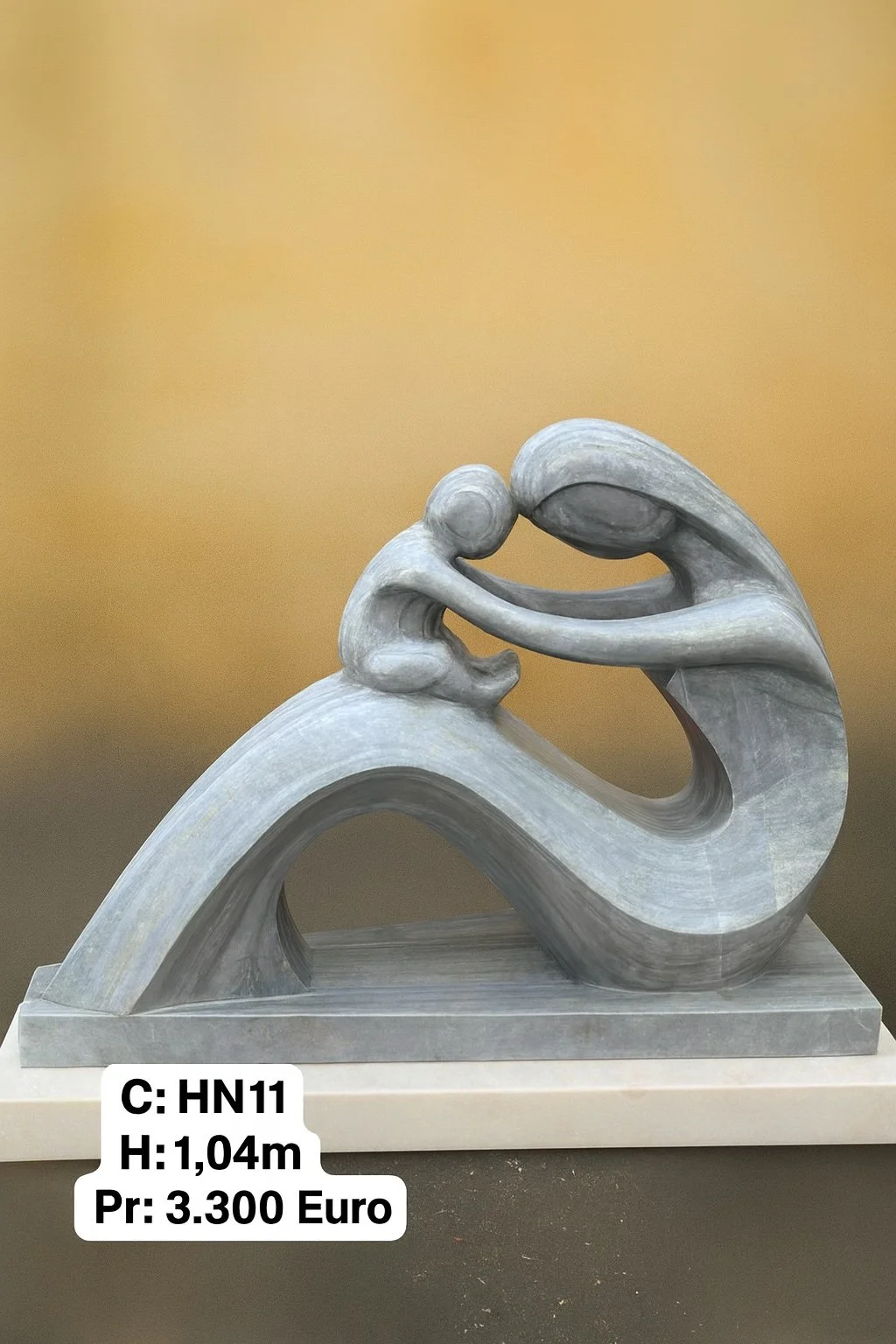 A sculpture of a human figure holding a child, both bending forward, made of gray material, possibly stone or metal, displayed on a rectangular base. There is a price tag indicating 3,300 Euros and dimensions of 1.04 meters high.