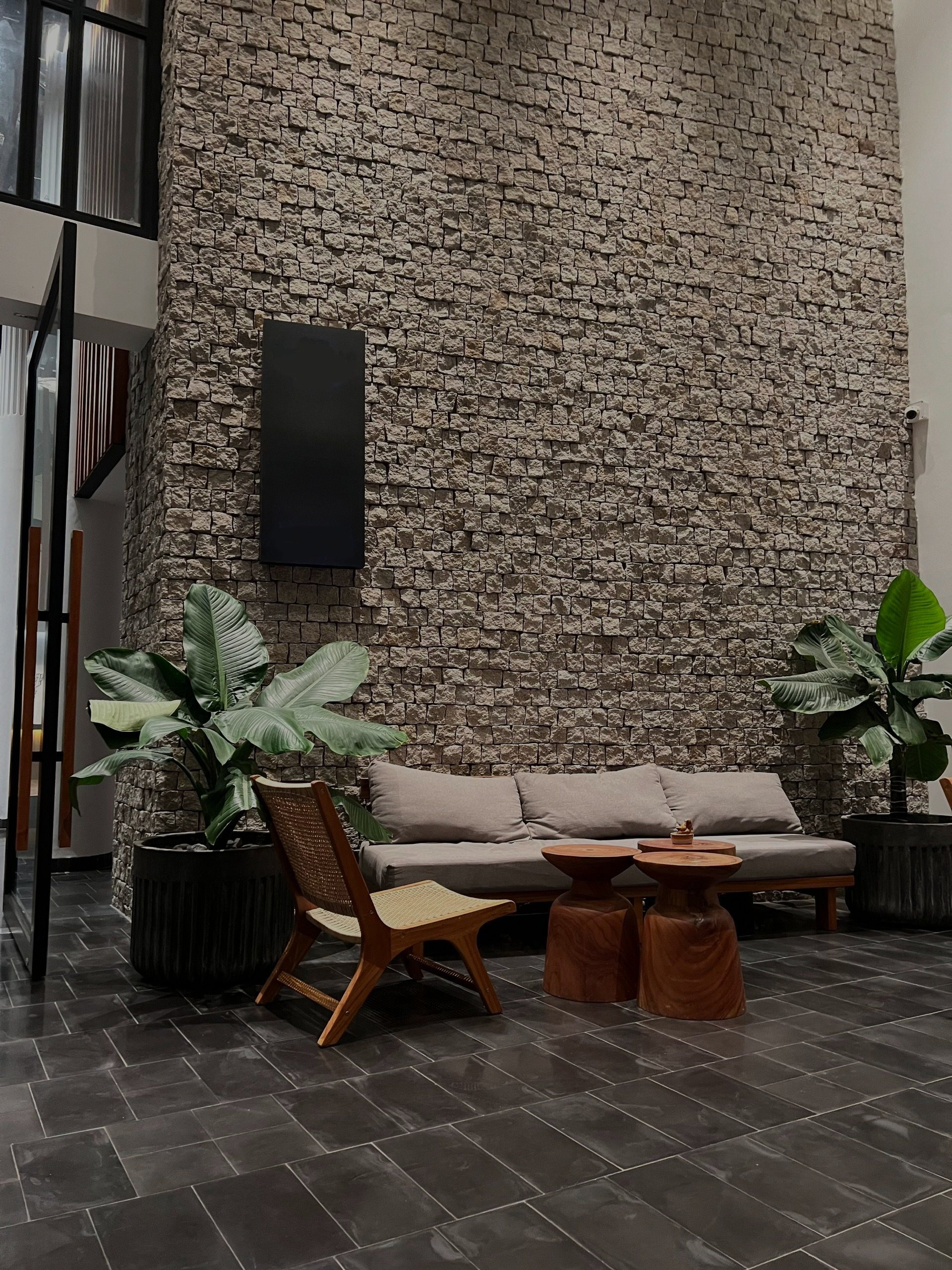 modern living room with stone wall, gray sofa, wooden chair, round wooden tables, and potted plants
