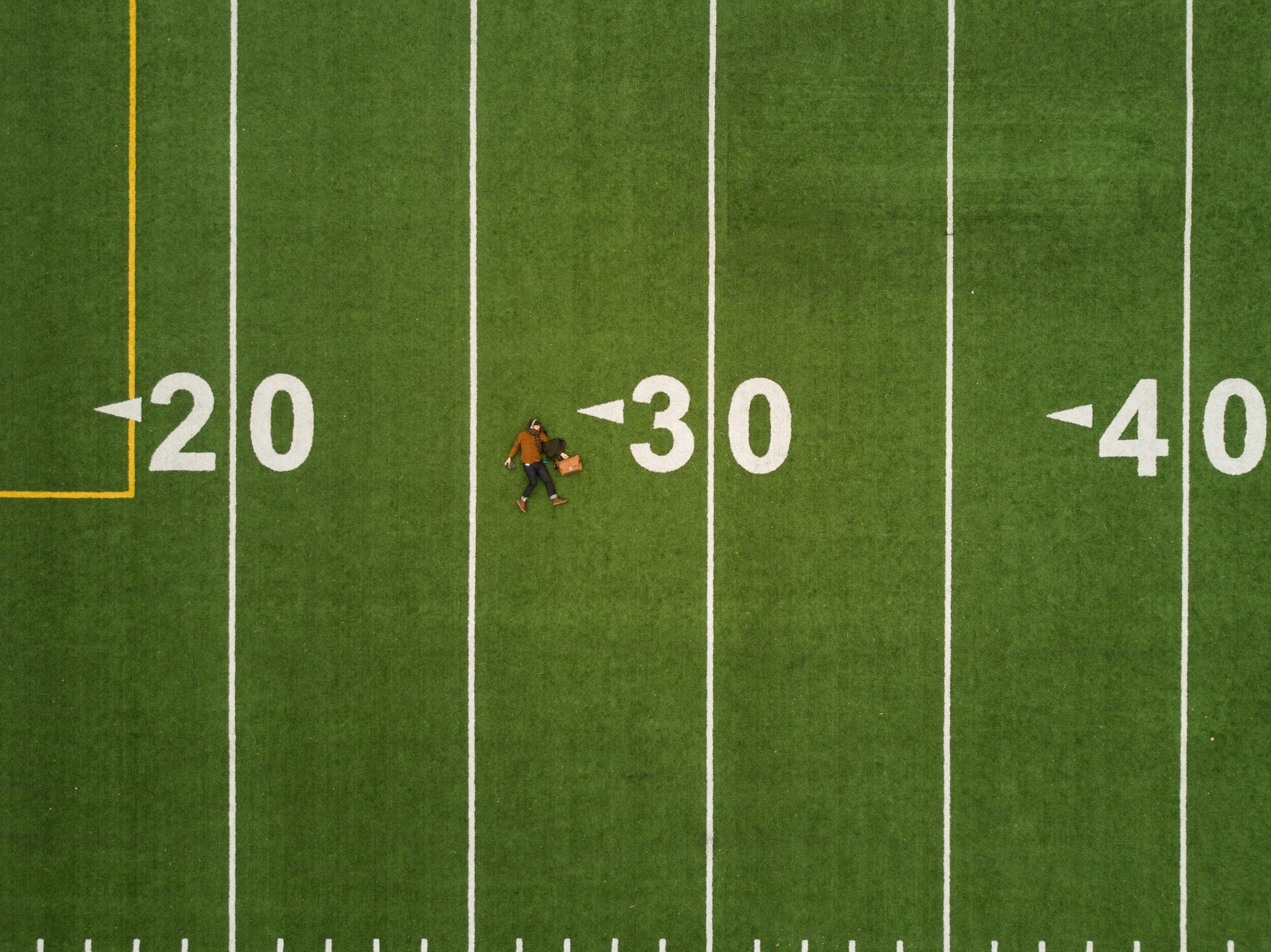 Bird eyes view of a man laying at the 25 yard line of a football field.