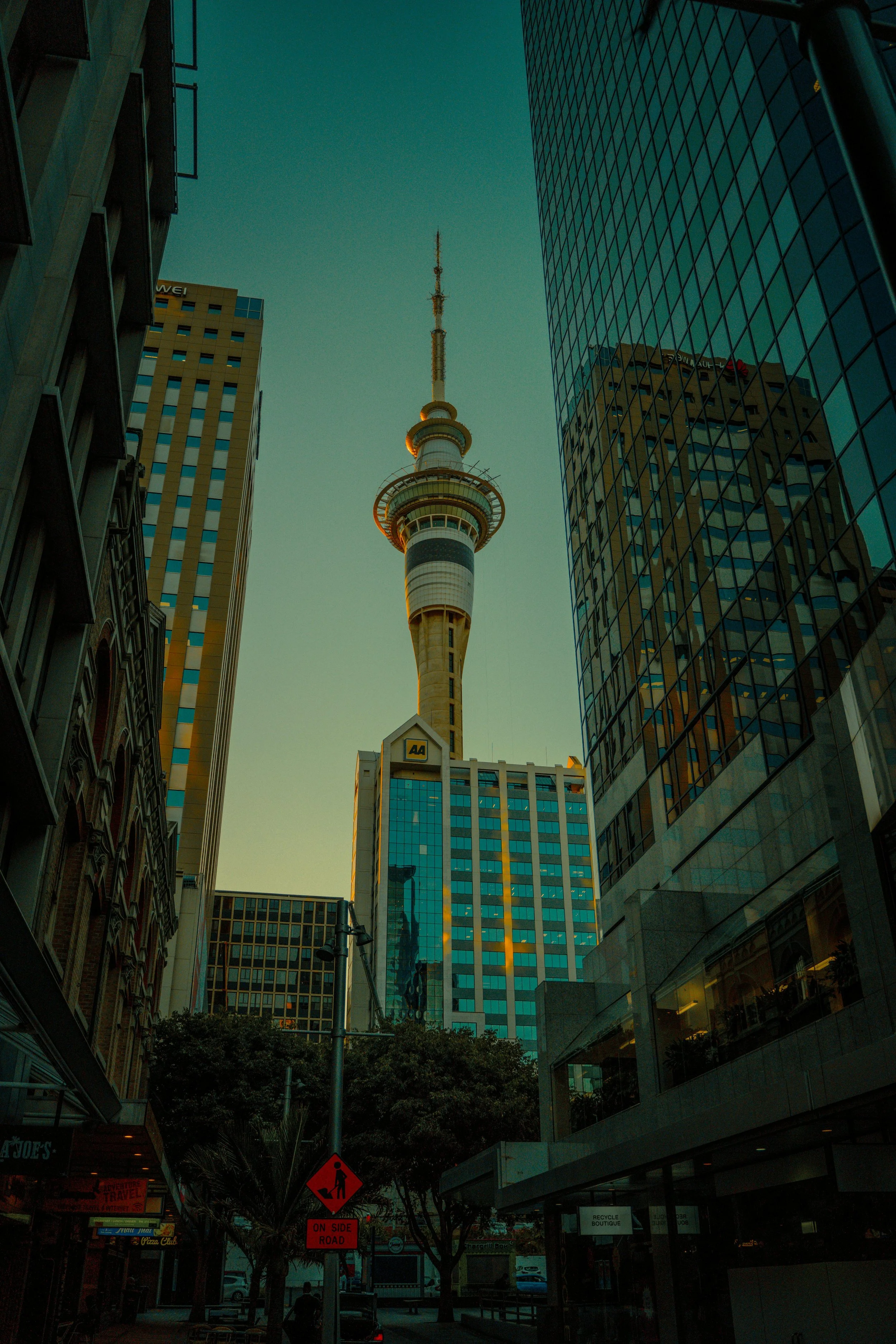Tall observation tower with a spire, surrounded by modern glass buildings and older brick structures in an urban cityscape.