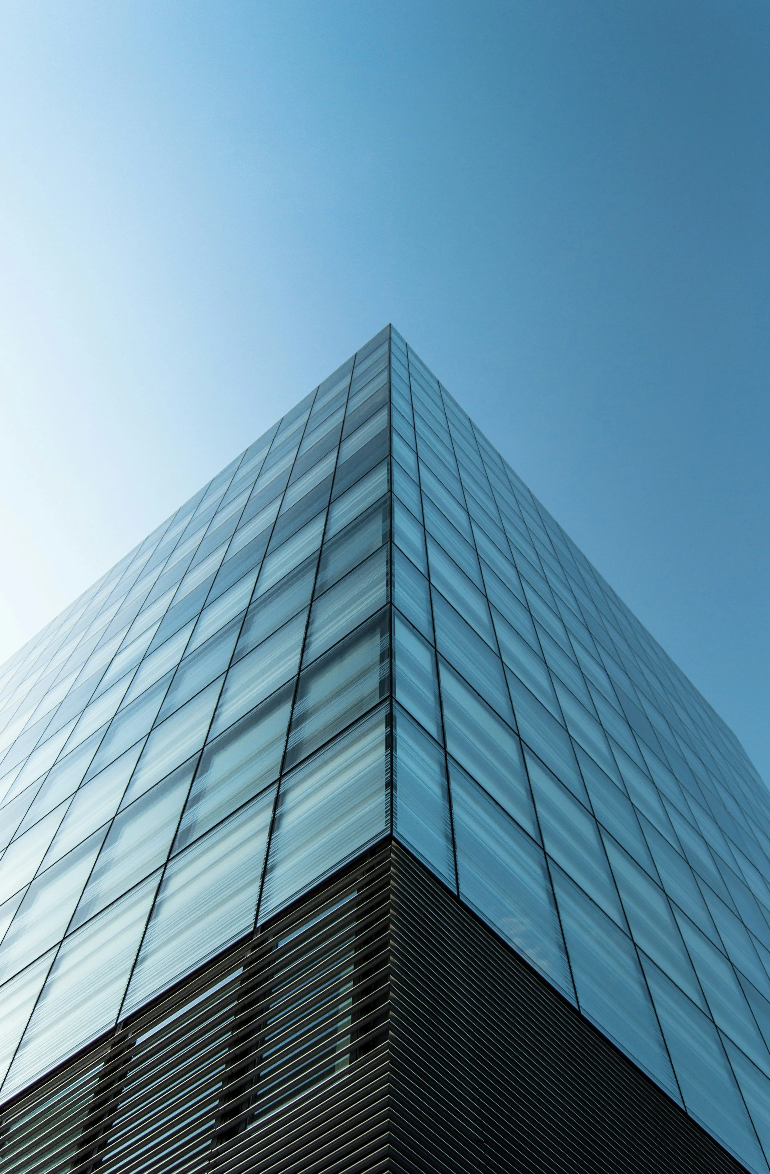 Low-angle view of a modern glass skyscraper against a clear blue sky.