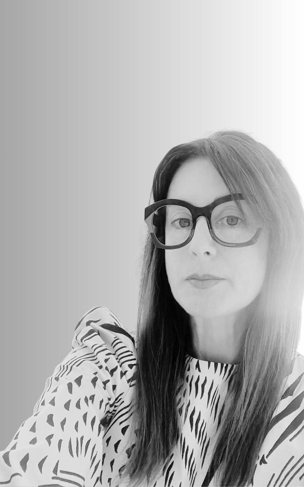 Black and white portrait of a woman with long hair, wearing large glasses and a patterned top.