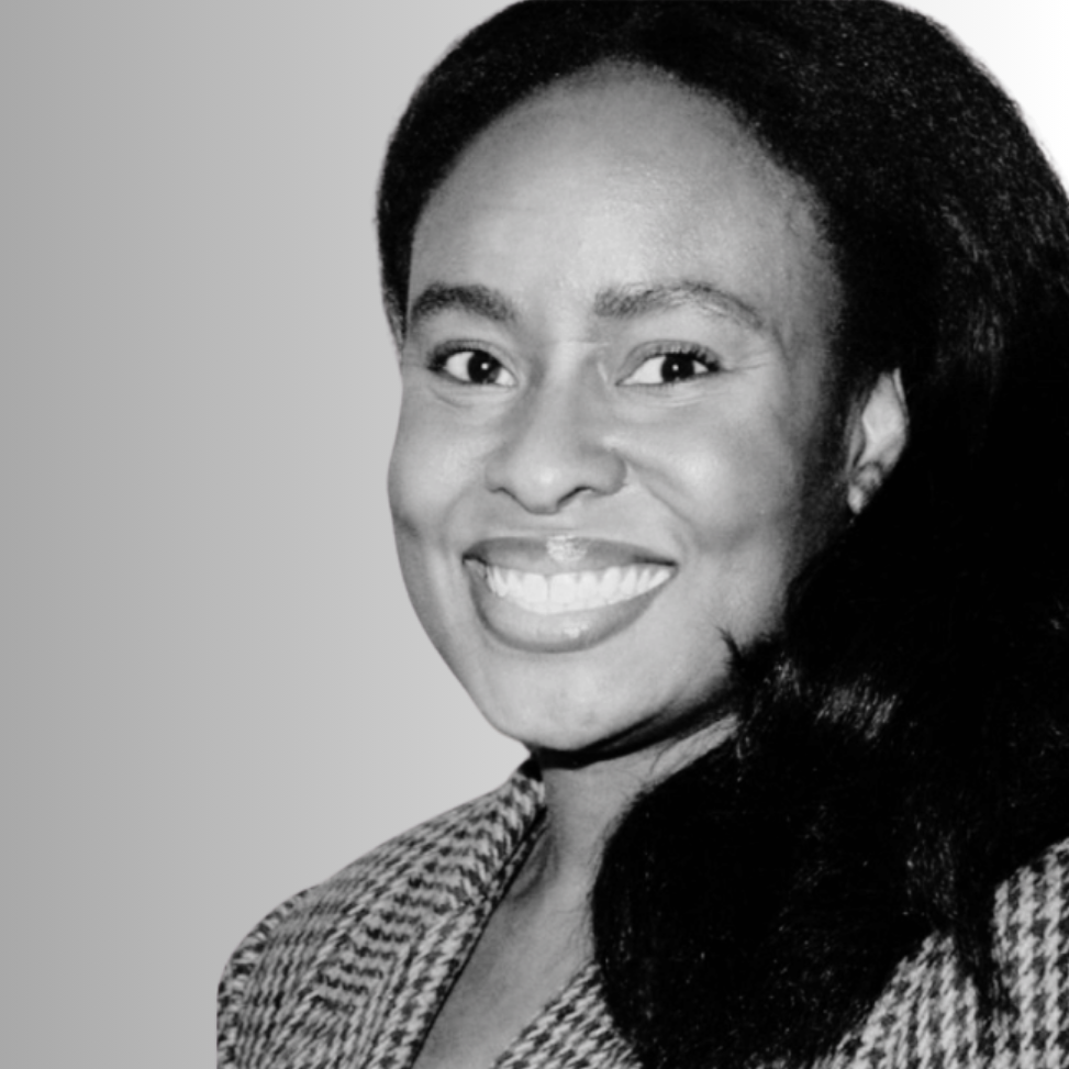 Black and white photo of a smiling woman with long, dark hair, wearing a patterned top.