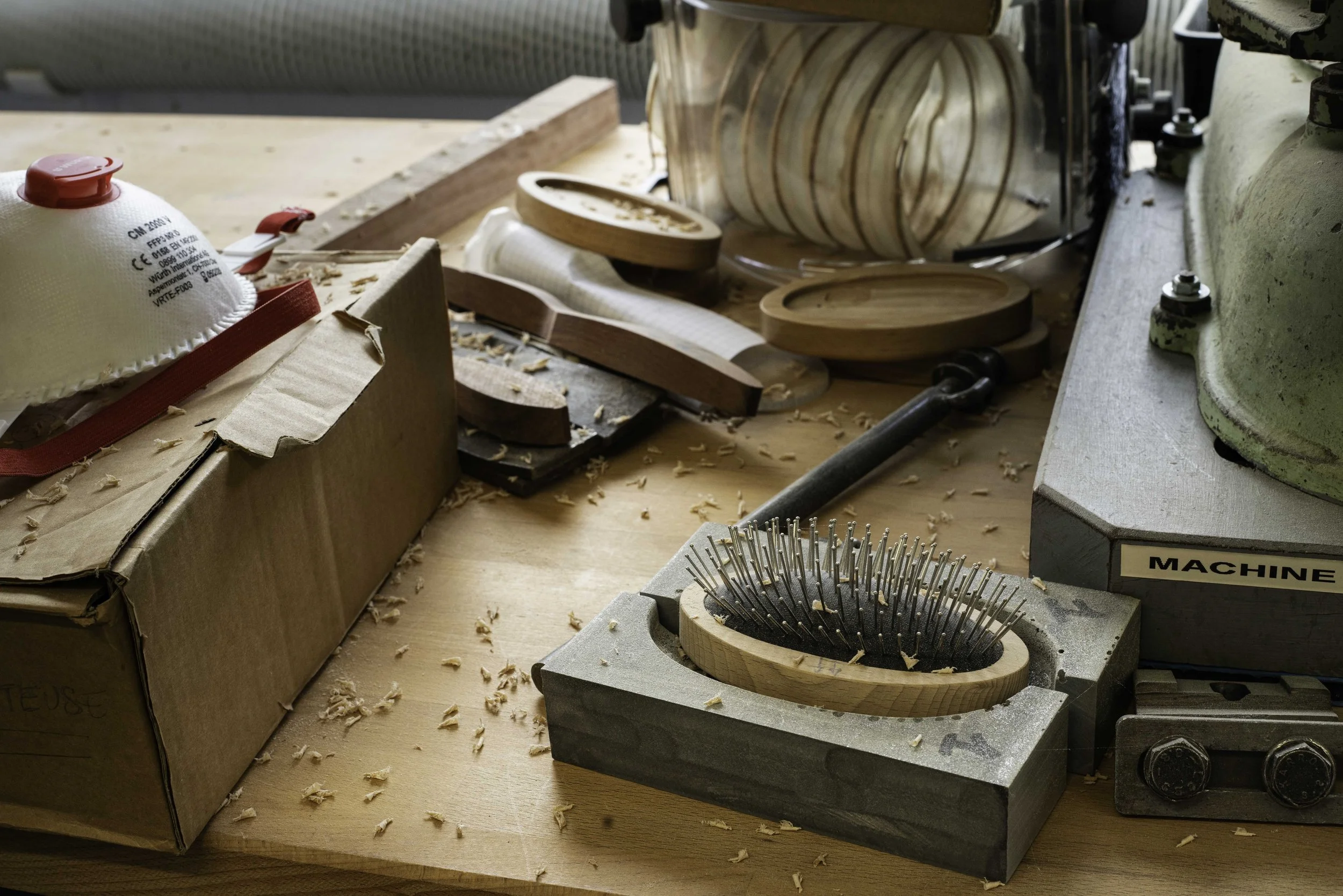 Woodworking workshop with various wooden pieces, tools, and a box of safety mask on a cluttered workbench.