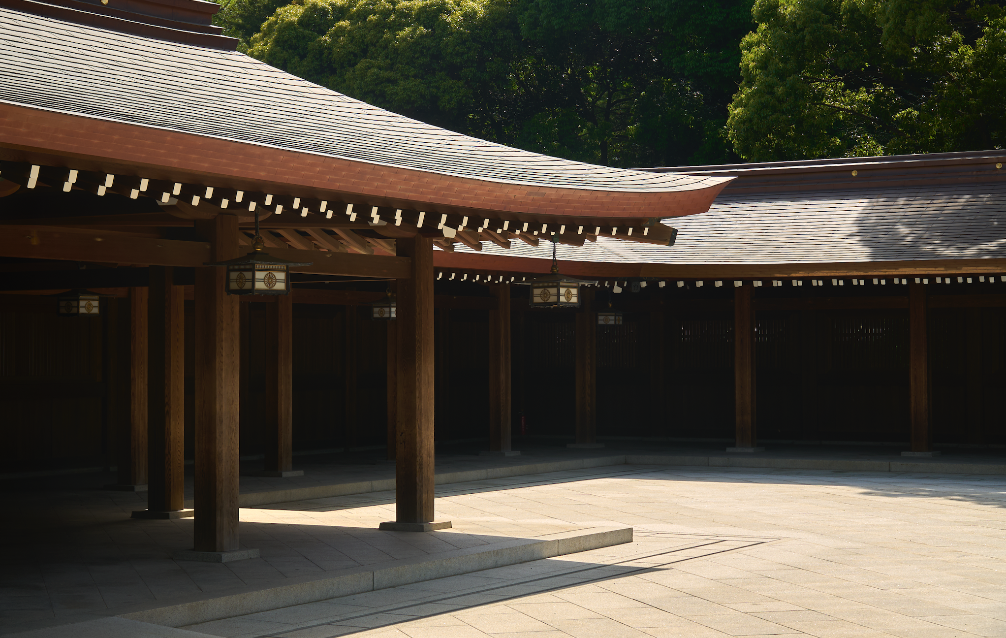 Traditional Japanese wooden structure with curved roofs, illuminated lanterns, and surrounded by lush green trees.