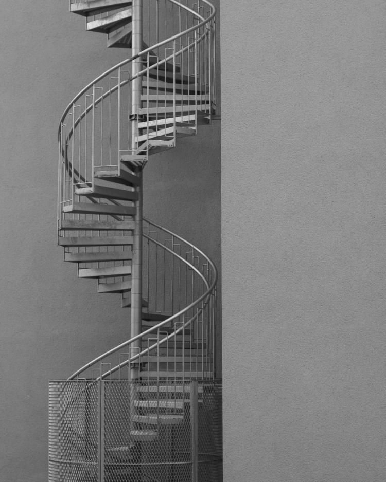 Black and white outdoor metal spiral staircase against a plain wall.