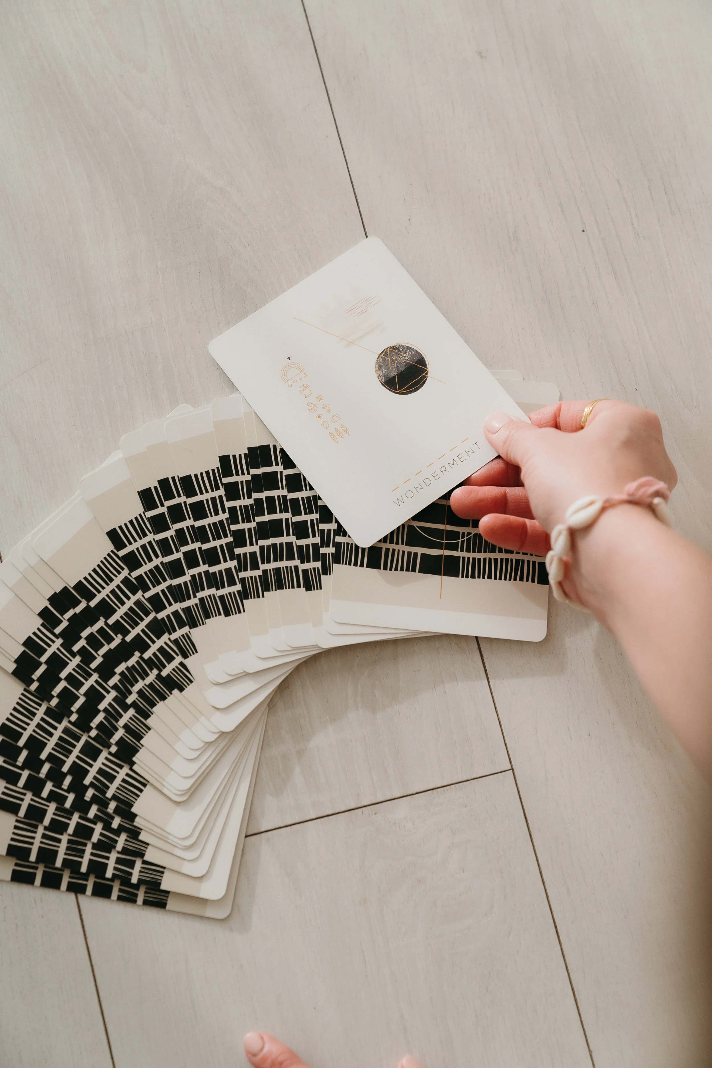 Person holding a tarot card labeled 'Wonderment' above a spread of cards on a light wooden floor.