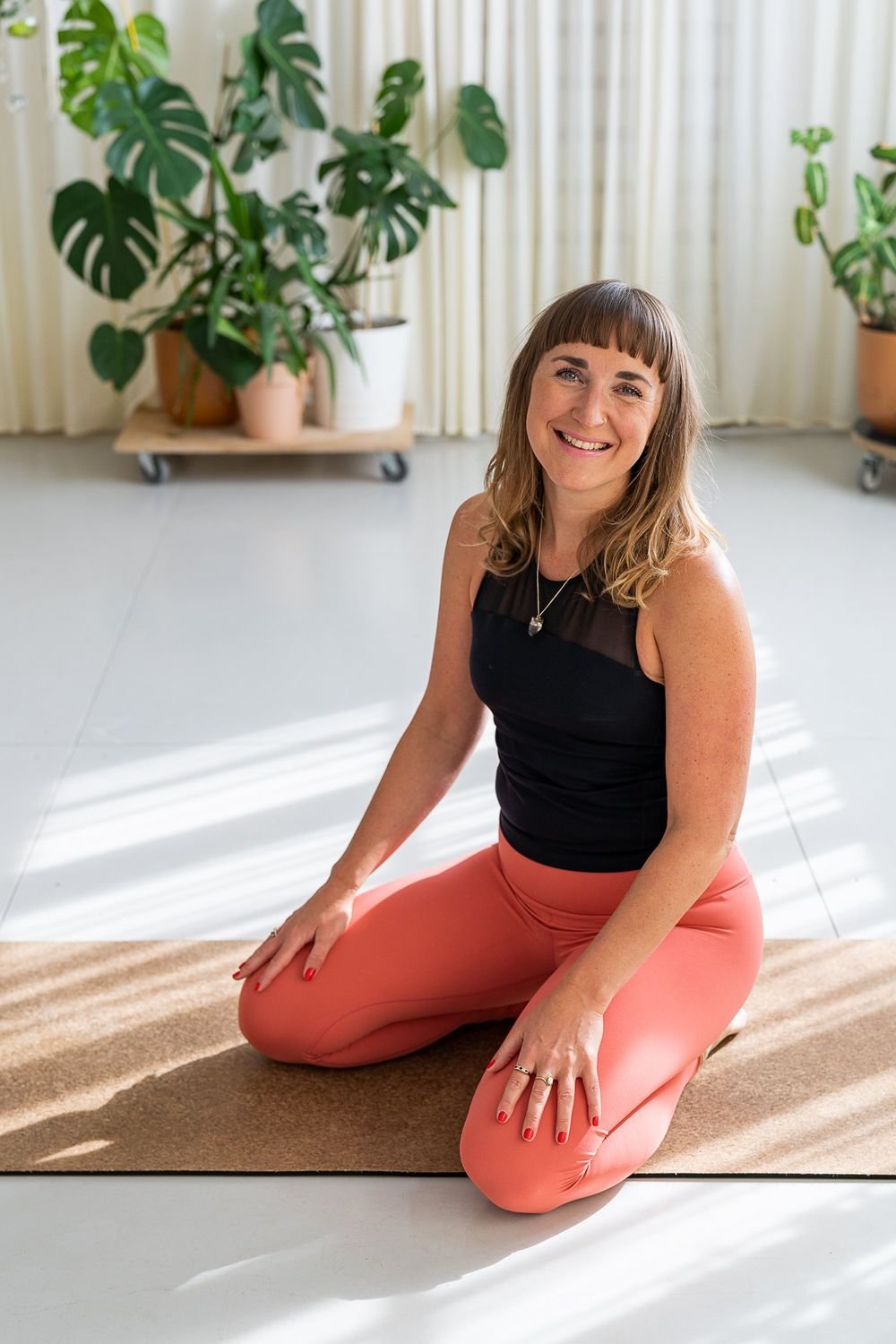 Dr Stephanie Minchin kneeling on a yoga mat in a sunlit room with plants