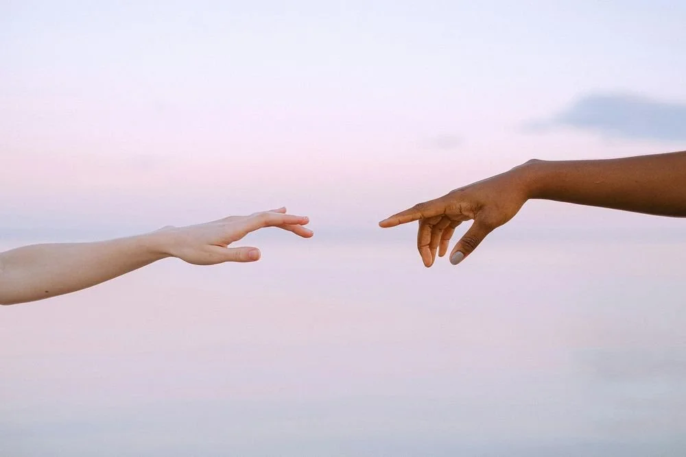 Two hands reaching towards each other against a pink sky