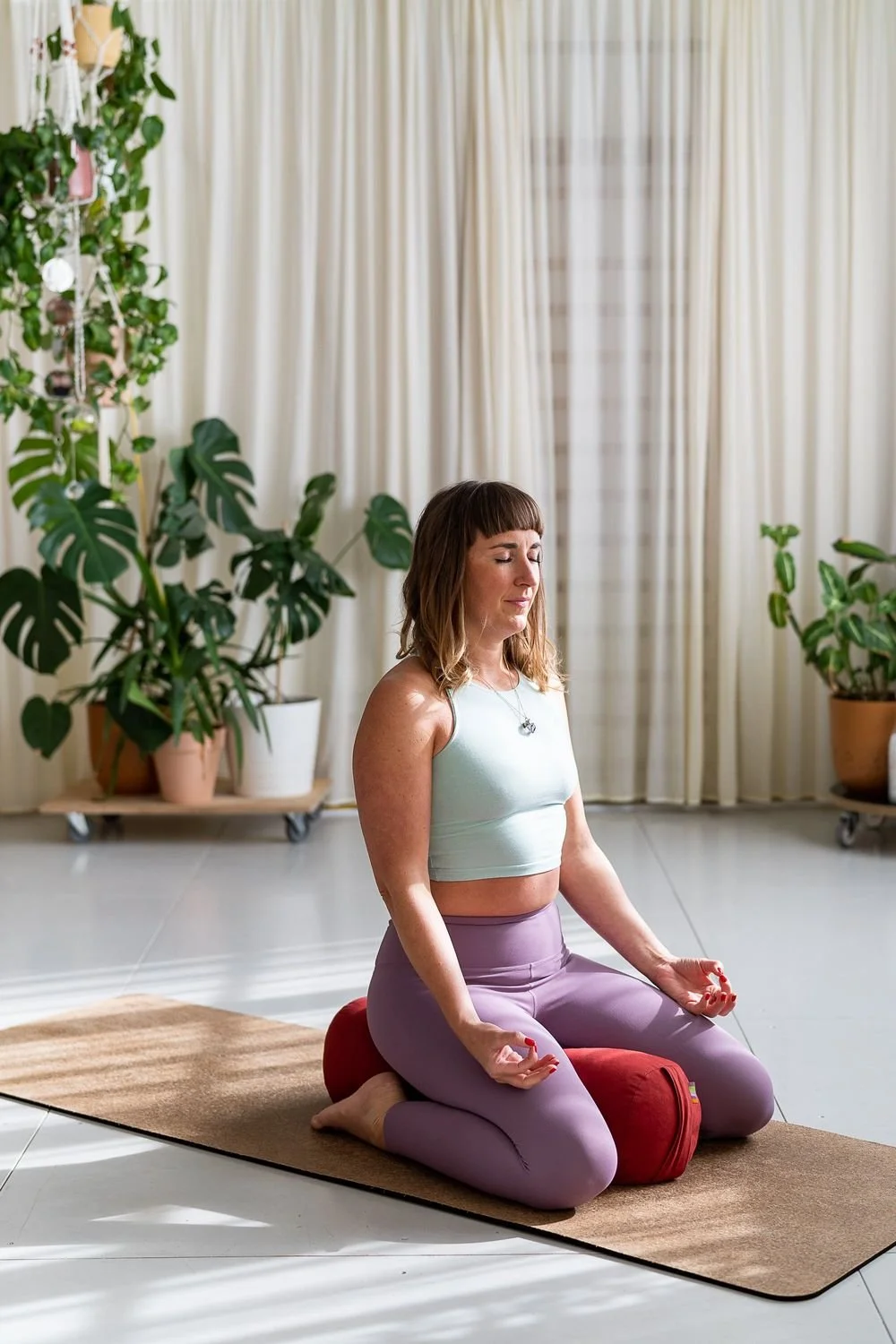 Dr Stephanie Minchin in seated meditation on a yoga mat in a plant filled room