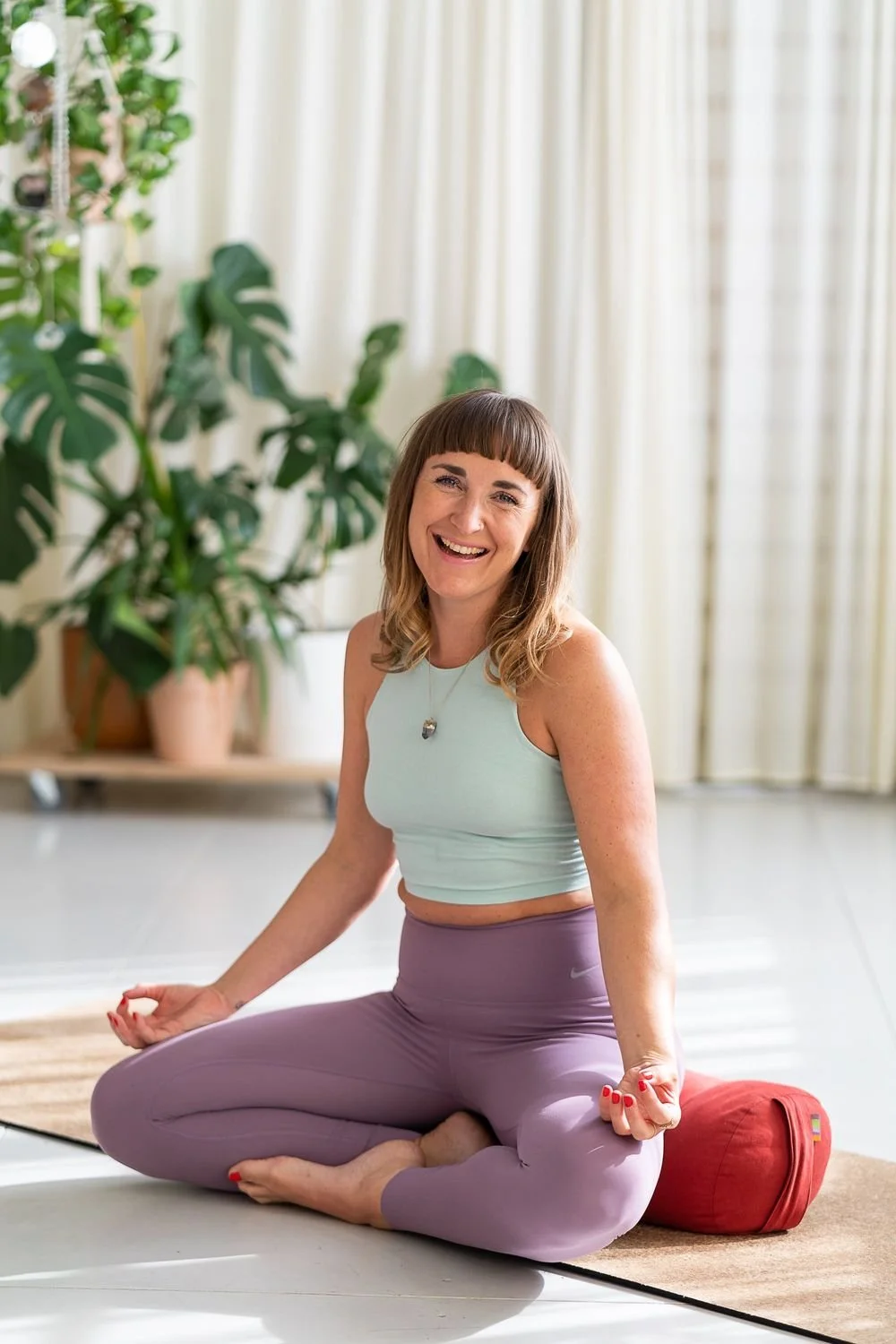 Dr Stephanie Minchin seated in meditation on a yoga mat in a plant filled studio