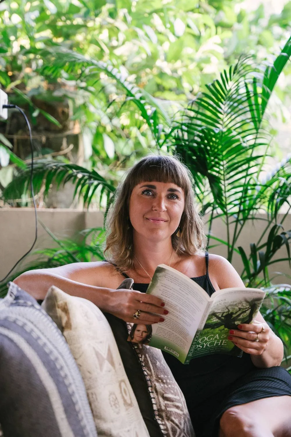 Dr Stephanie Minchin reading a book on a sofa surrounded by plants