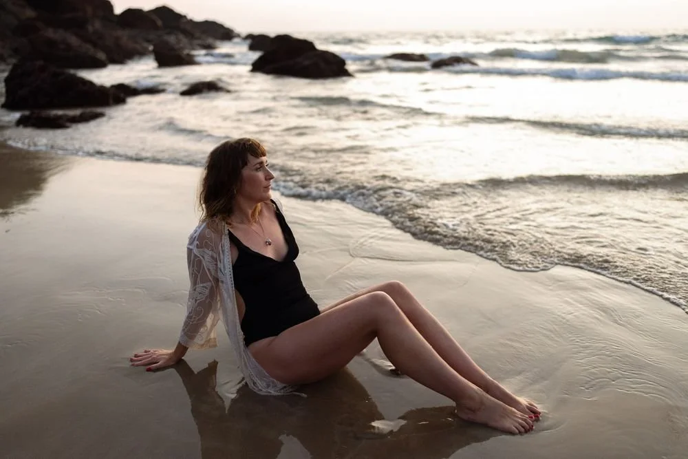 Dr Stephanie Minchin sitting at the water's edge on a beach at sunrise