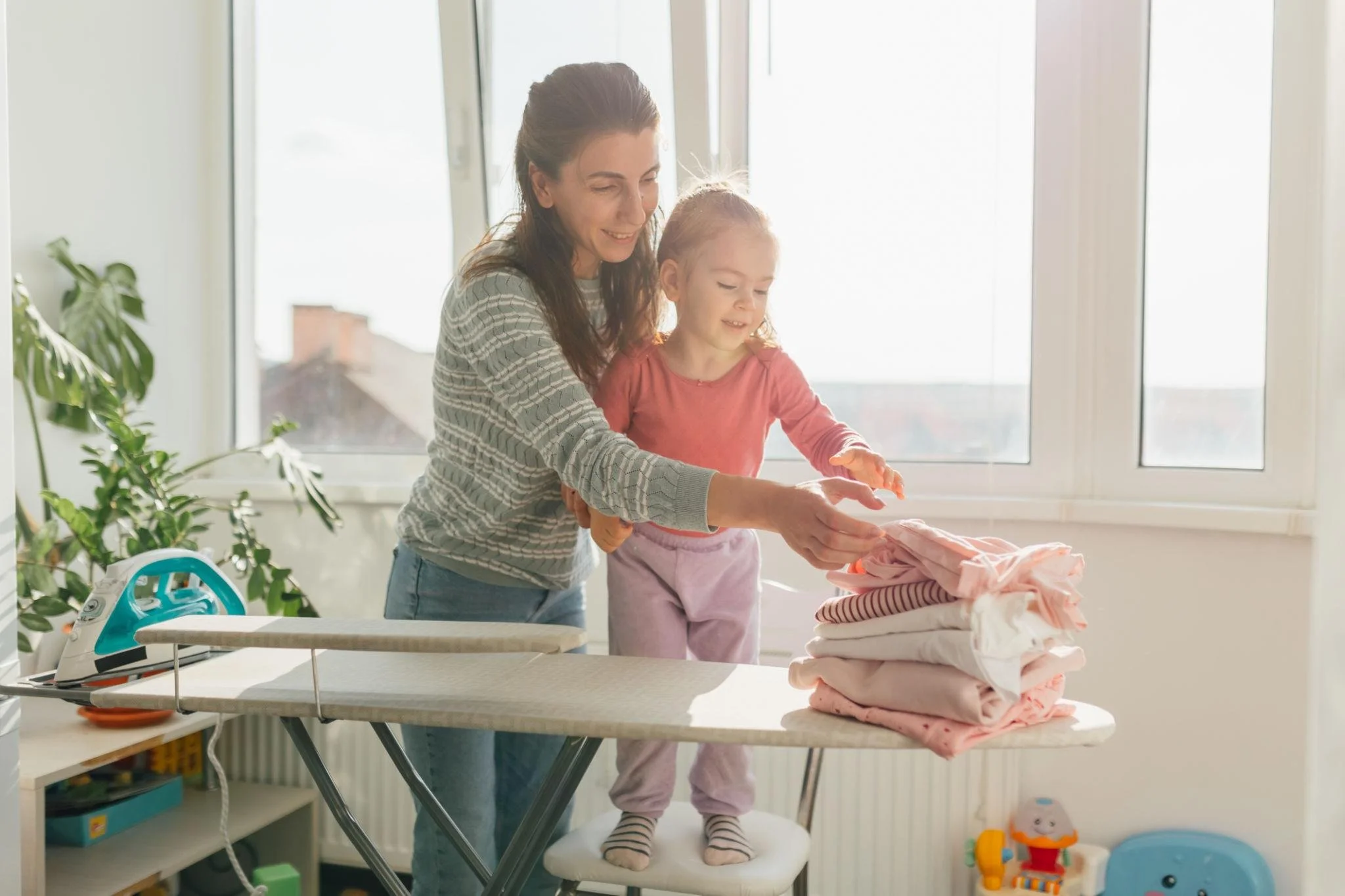 Parent folding laundry with a toddler while talking together during an everyday speech and language activity at home in Leander, Texas.