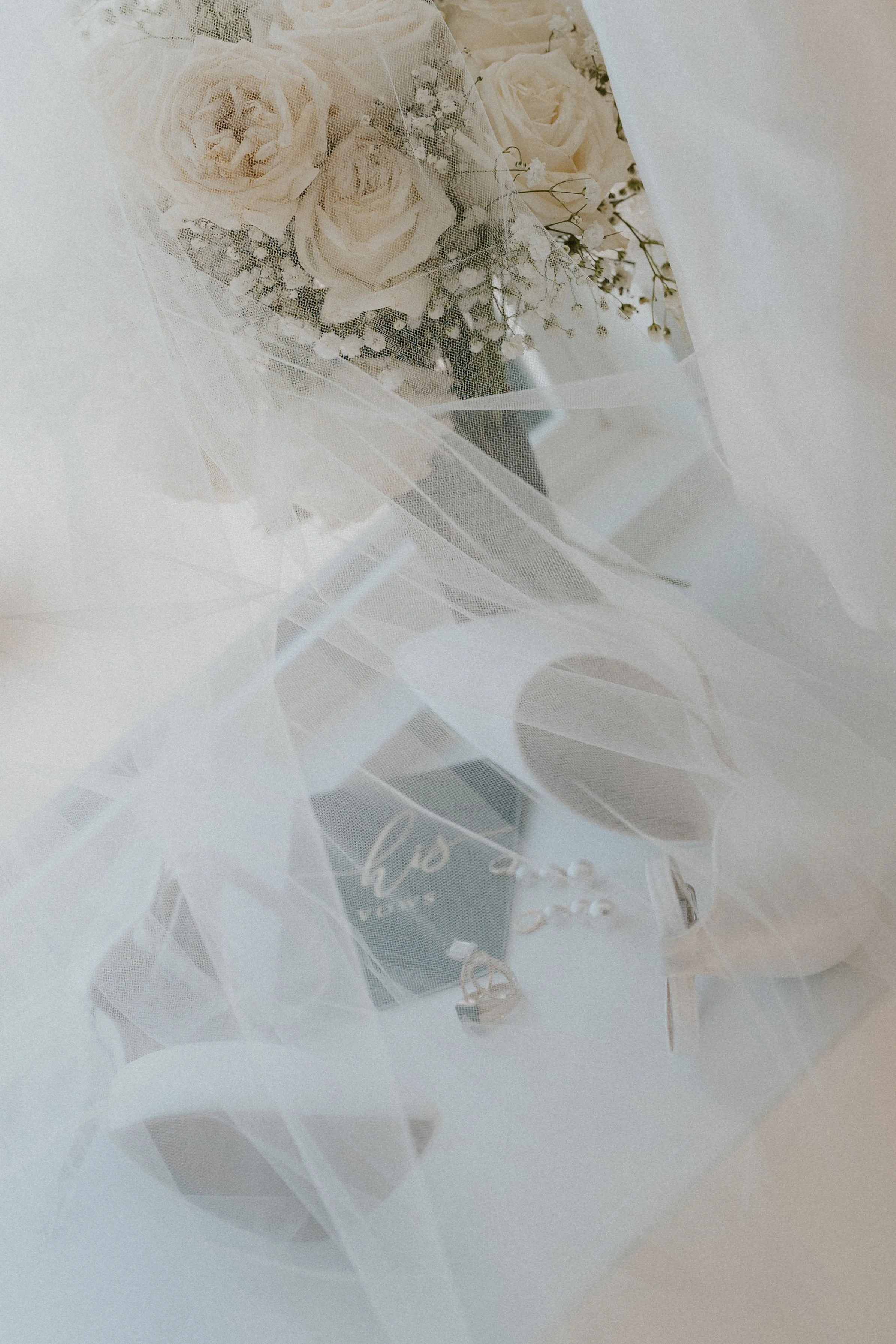 A bouquet of white roses and small white flowers wrapped in sheer white fabric.