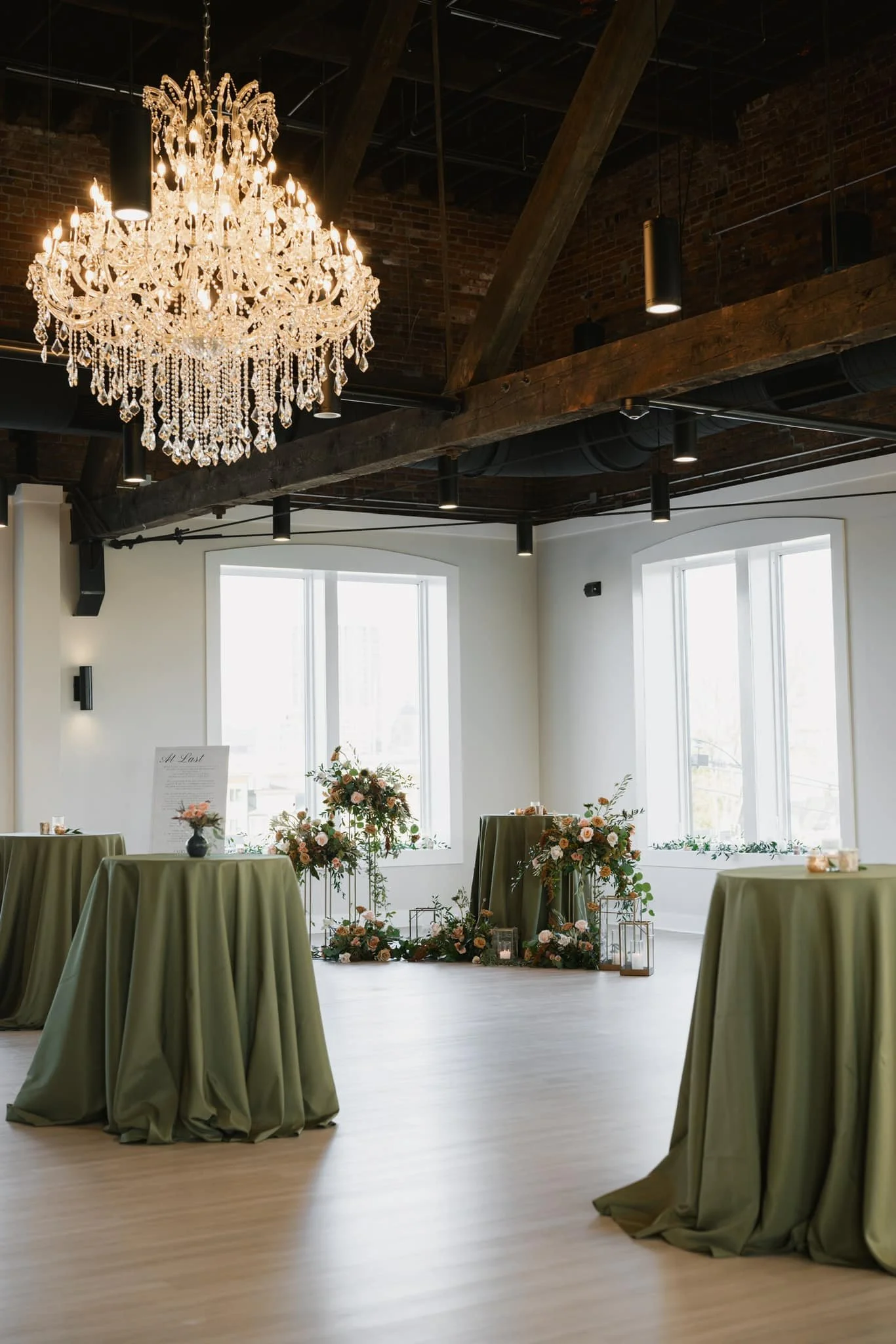 Elegant indoor event space with a crystal chandelier, four round tables with green tablecloths, and floral arrangements