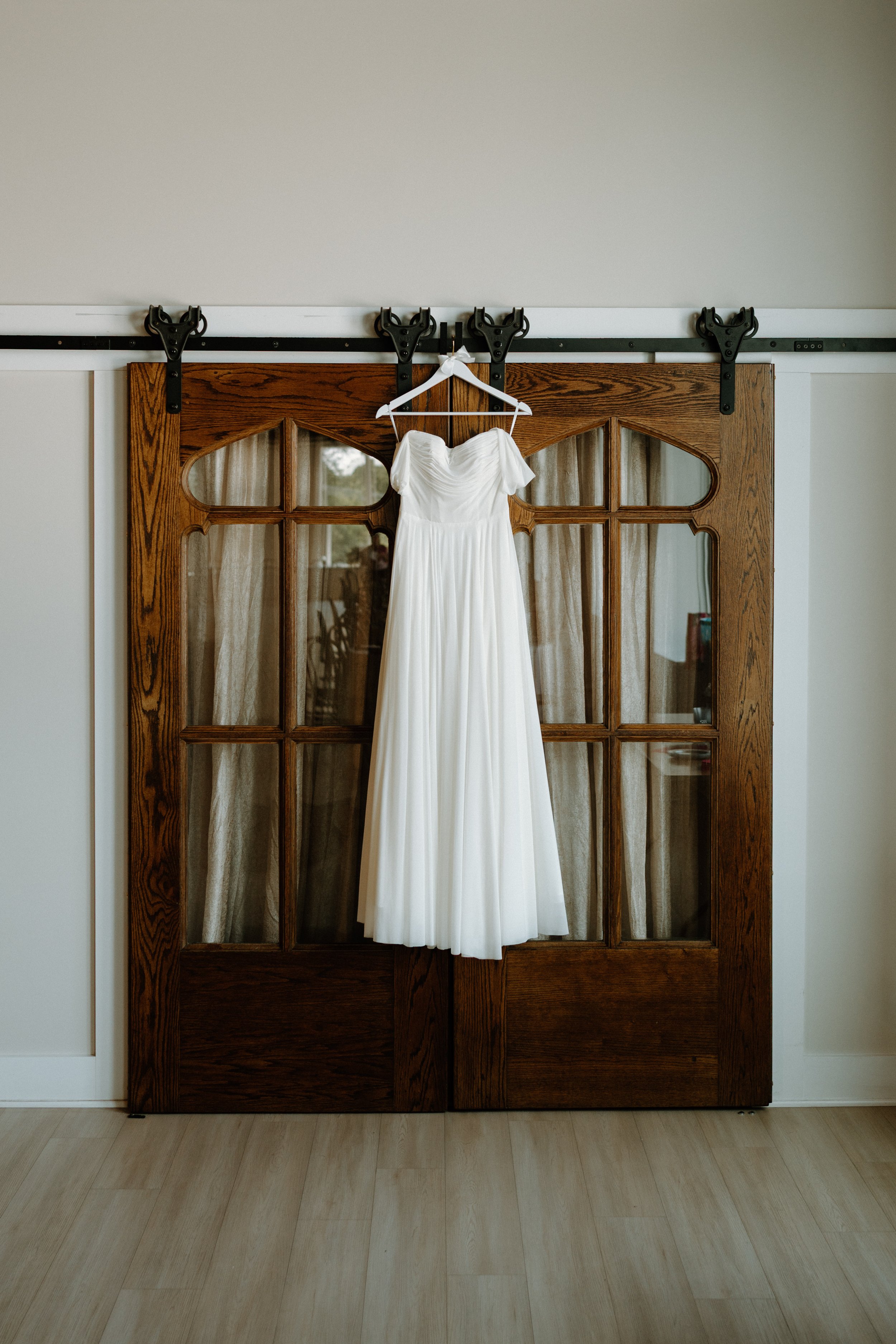A white wedding dress hanging on a white hanger on a wooden sliding door with glass panels.
