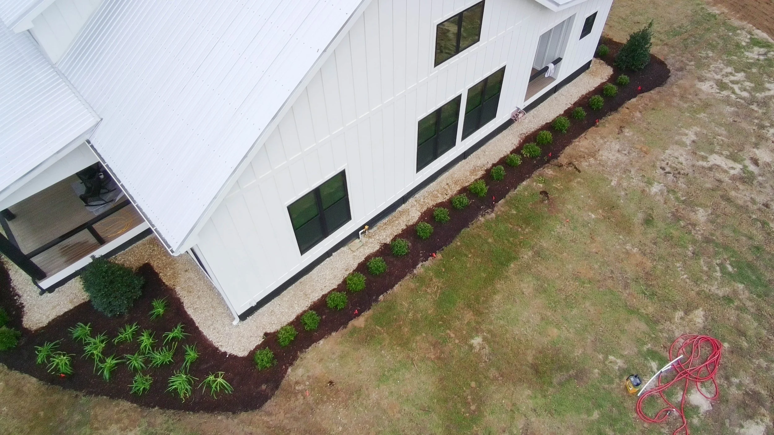 drone picture of side of house lined with bushes. rock border against house