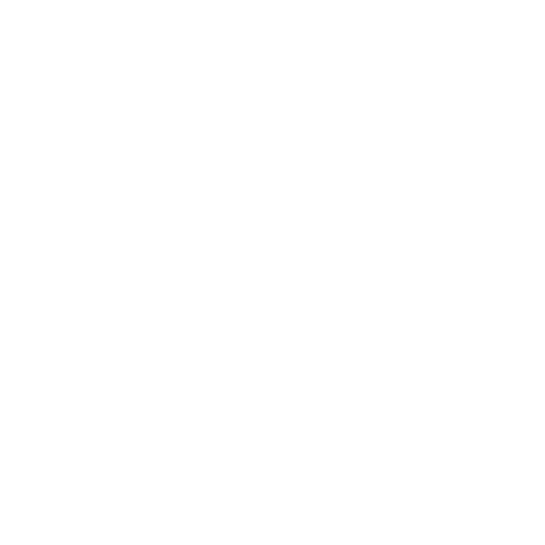 A woman standing outdoors in front of a brick building with white window frames, smiling and dressed in a black blazer, white top, beige high-waisted skirt, and dark tights.