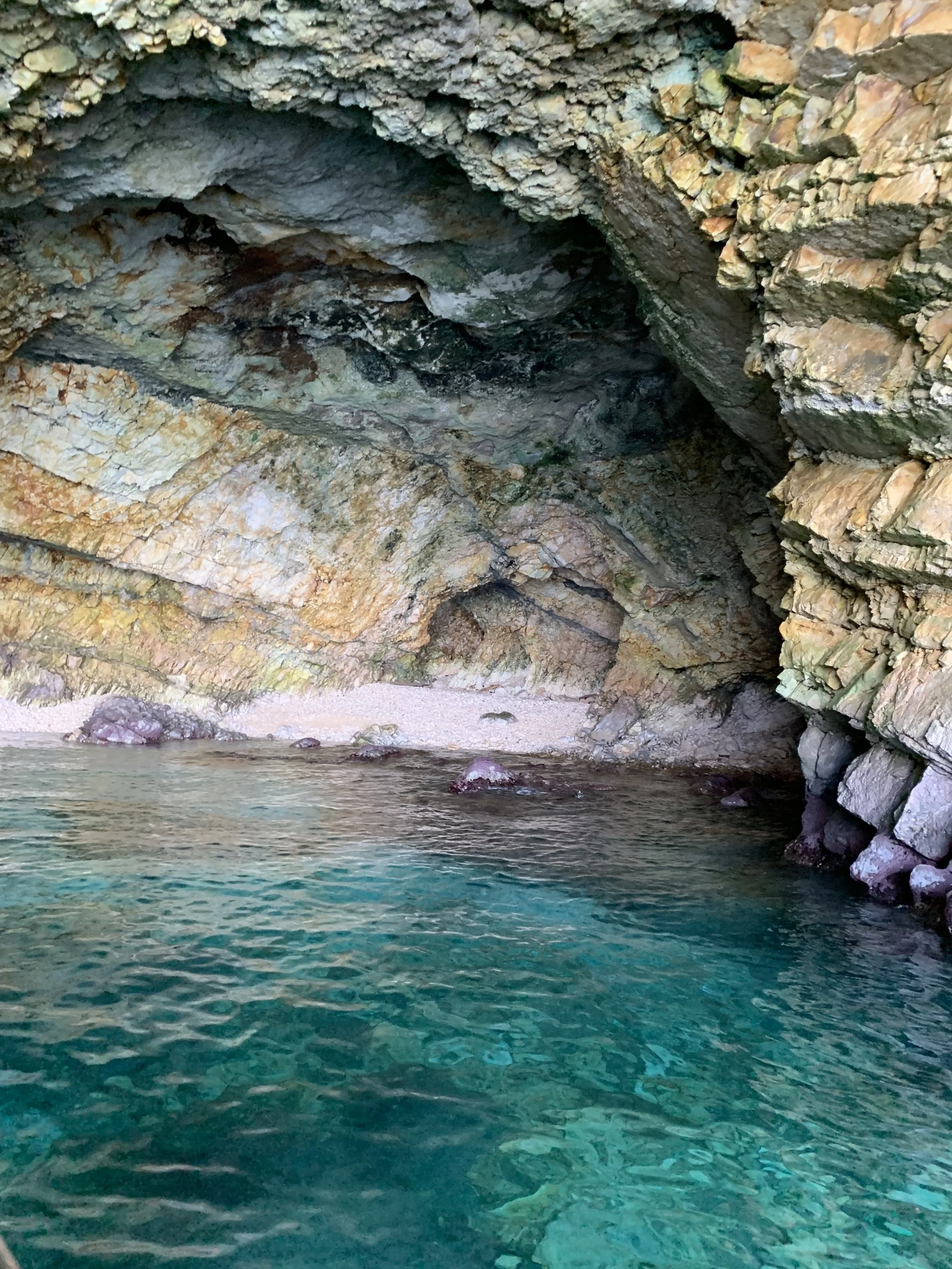 A rocky sea cave with clear turquoise water and a small sandy beach inside.
