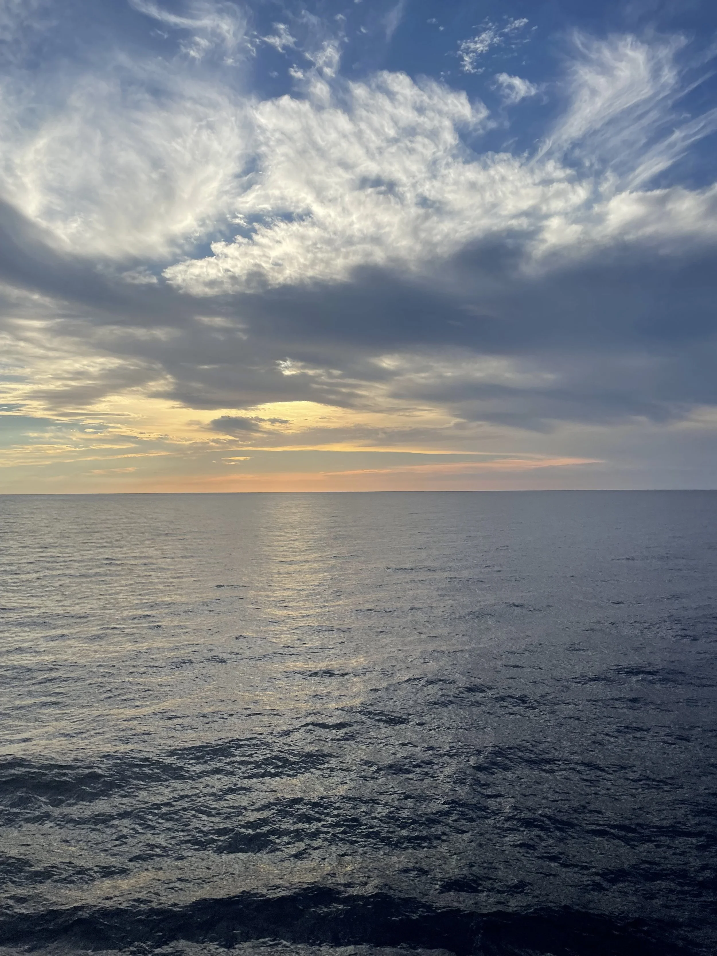 View of the ocean at sunset with a partly cloudy sky.