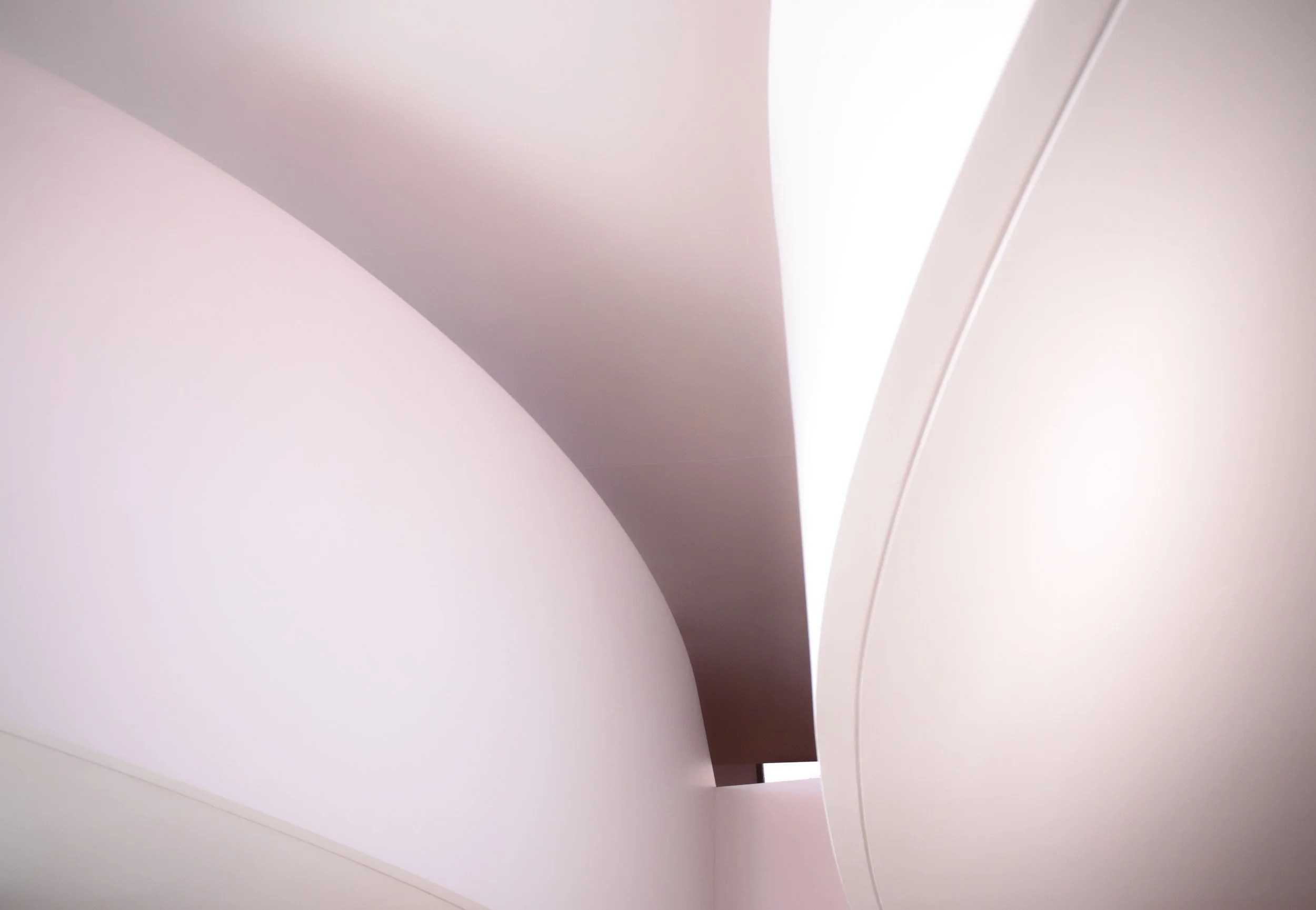 Abstract close-up of curved white architectural surfaces with soft pink lighting