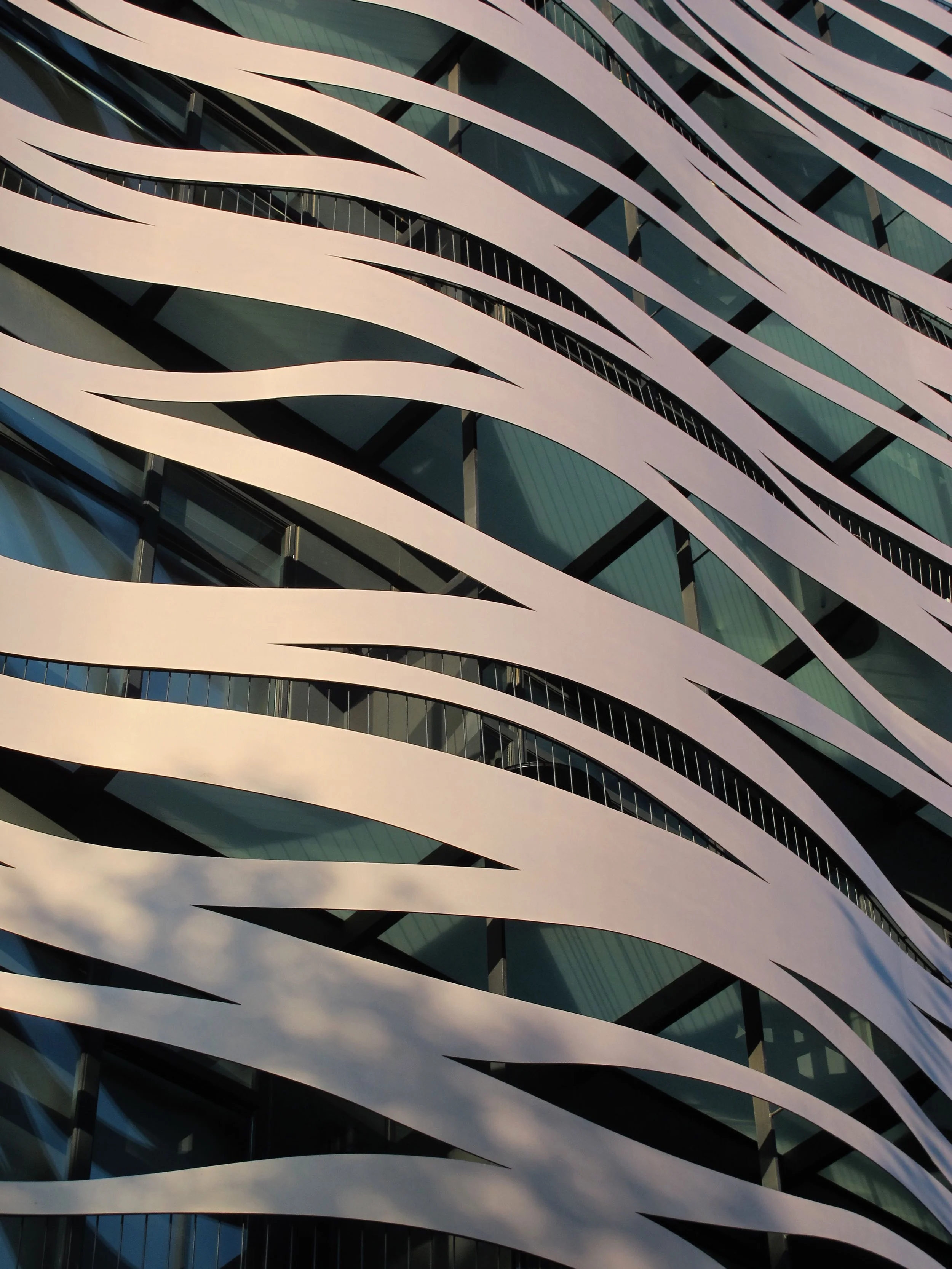 Close-up view of a modern building facade with sweeping white bands and dark reflective glass windows.