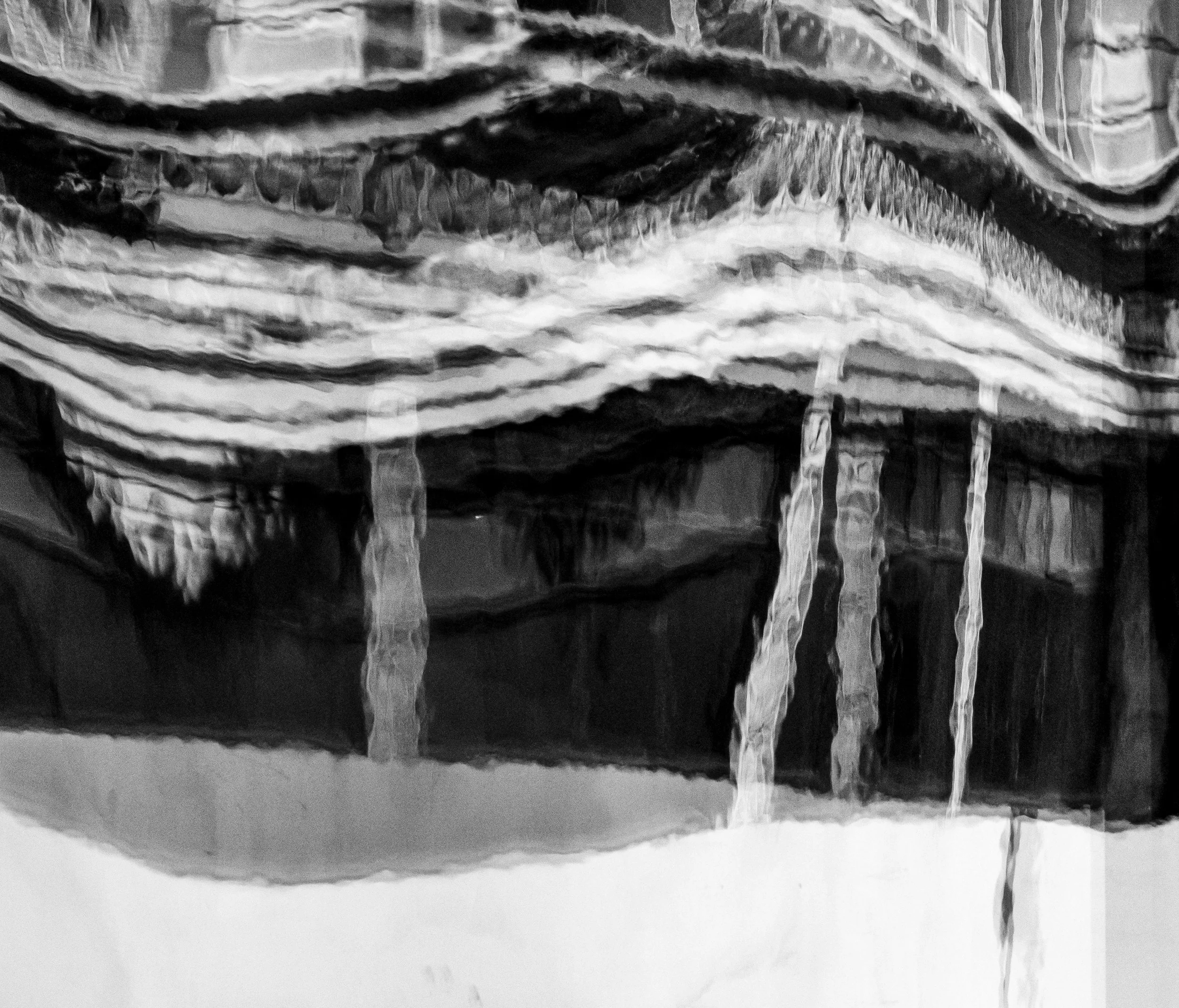 Black-and-white close-up of icicles hanging from layered snow and ice.