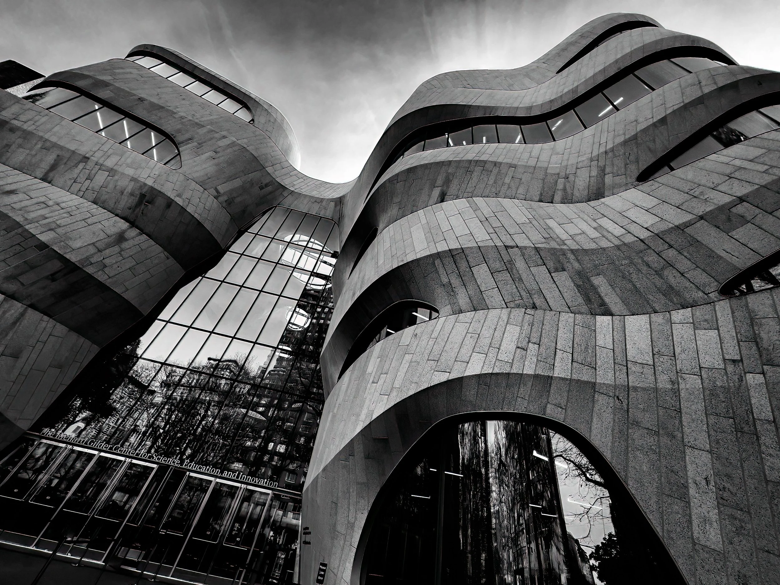 Black-and-white low-angle view of the Richard Gilder Center for Science, Education, and Innovation’s sculptural stone arches and curved glass facade