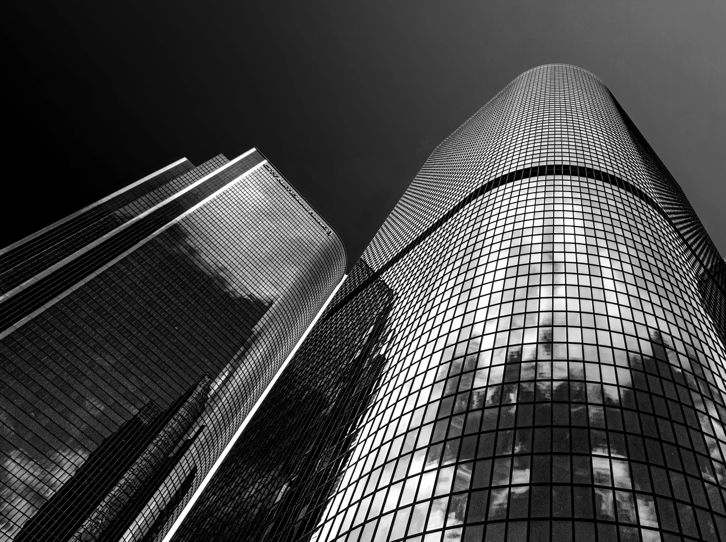 Black-and-white low-angle view of modern glass skyscrapers with curved facades against a dark sky