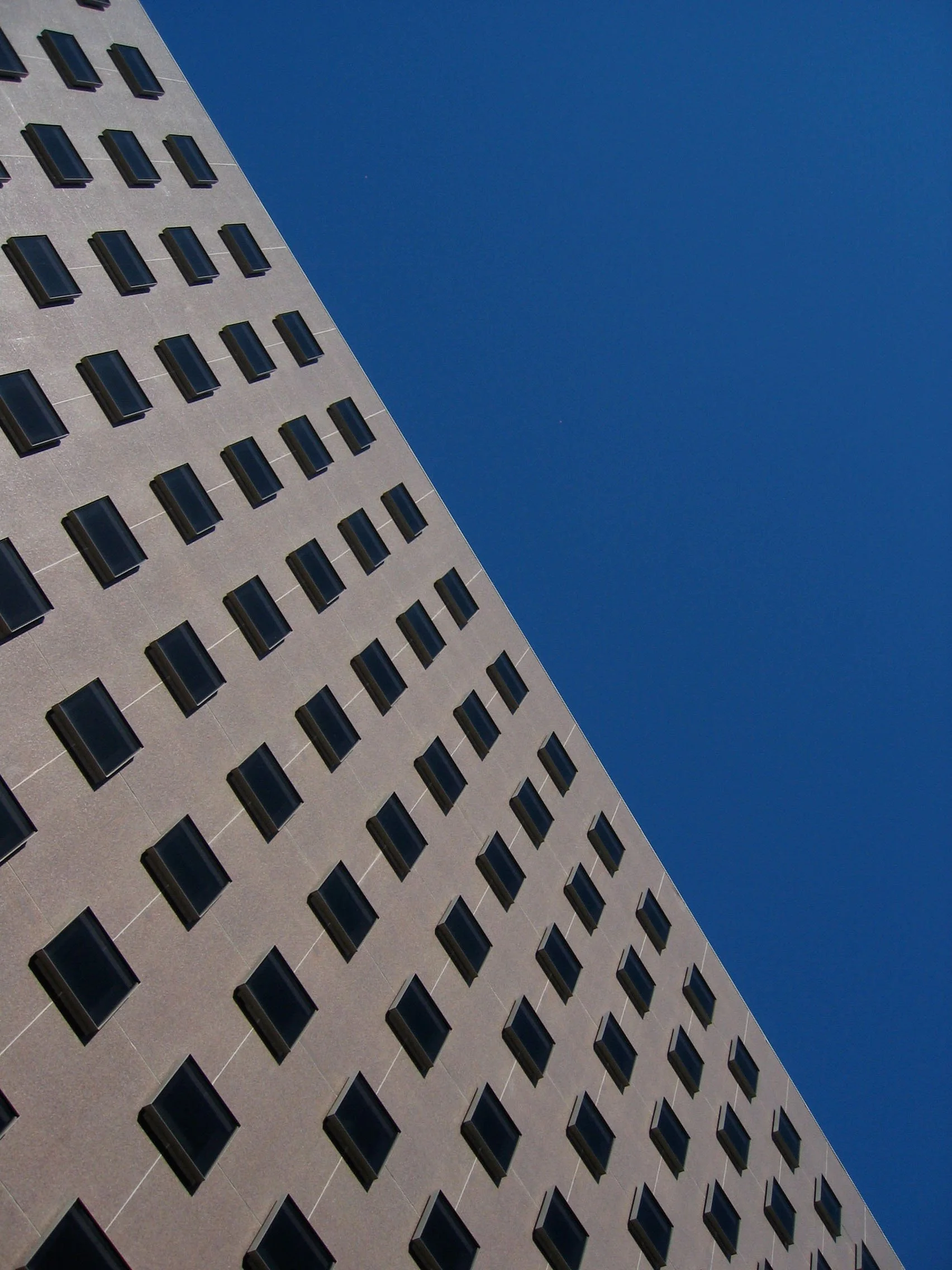 Upward view of a modern high-rise building with rows of dark windows against a clear blue sky