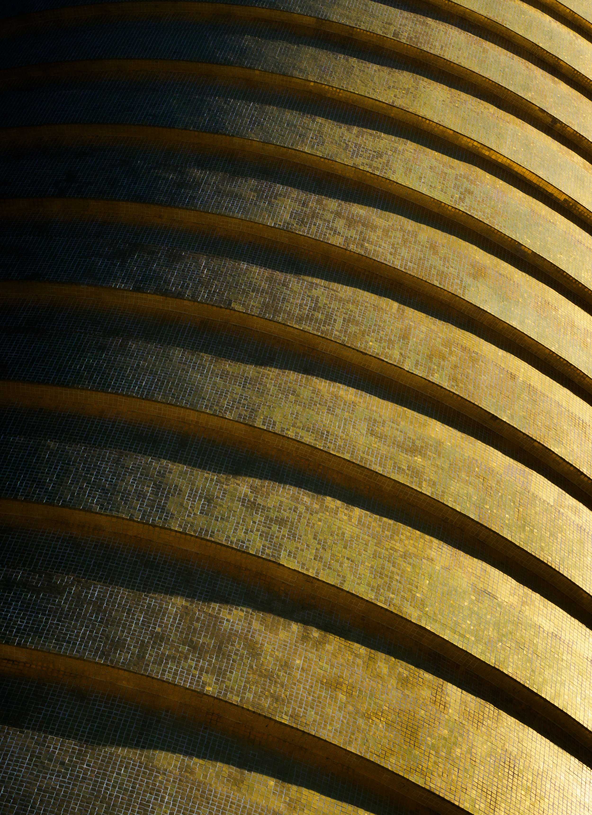 Abstract close-up of curved golden-brown and dark blue tiled architectural surfaces forming repeating wave patterns