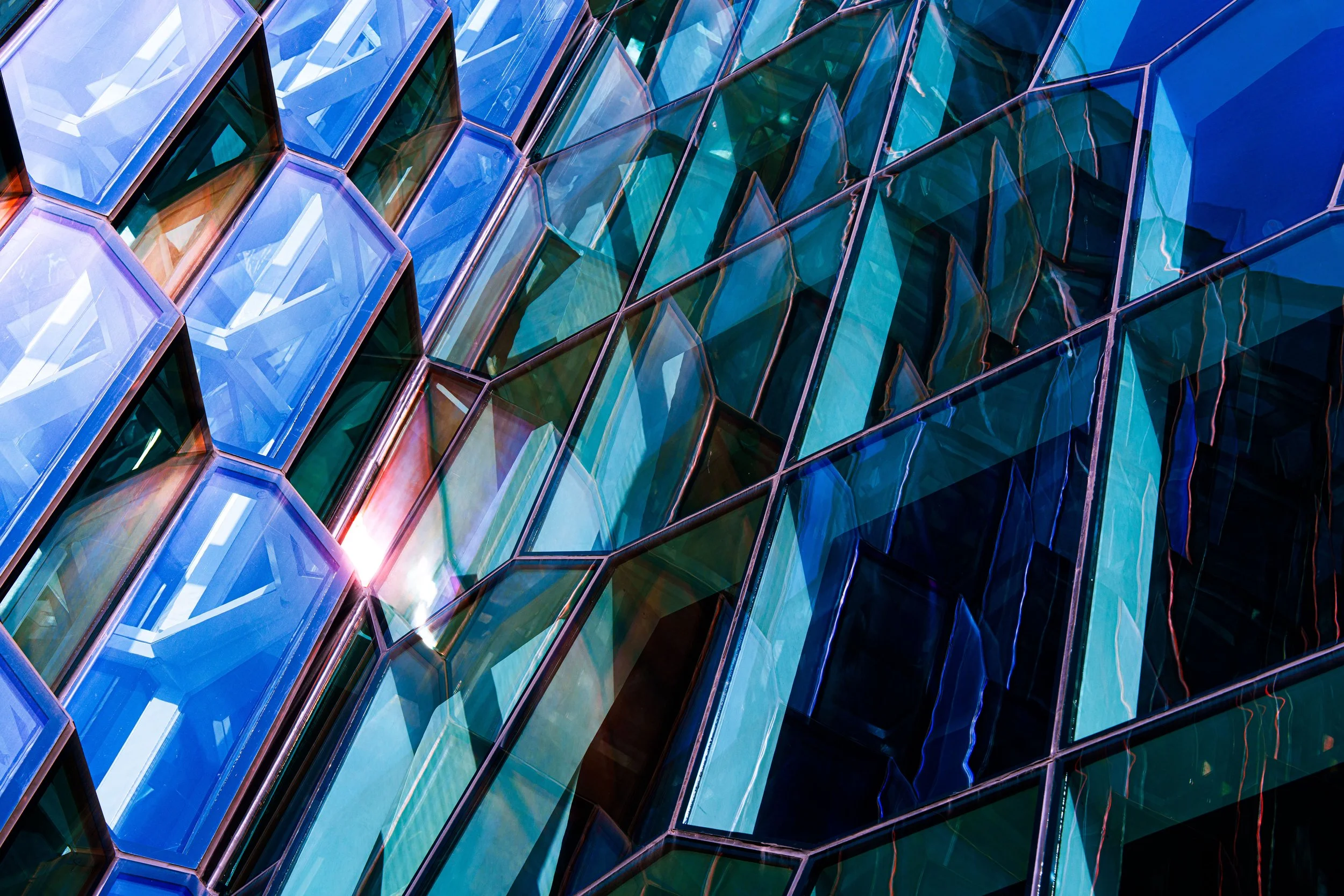 Abstract close-up of faceted blue and teal glass panels with geometric reflections and sunlight
