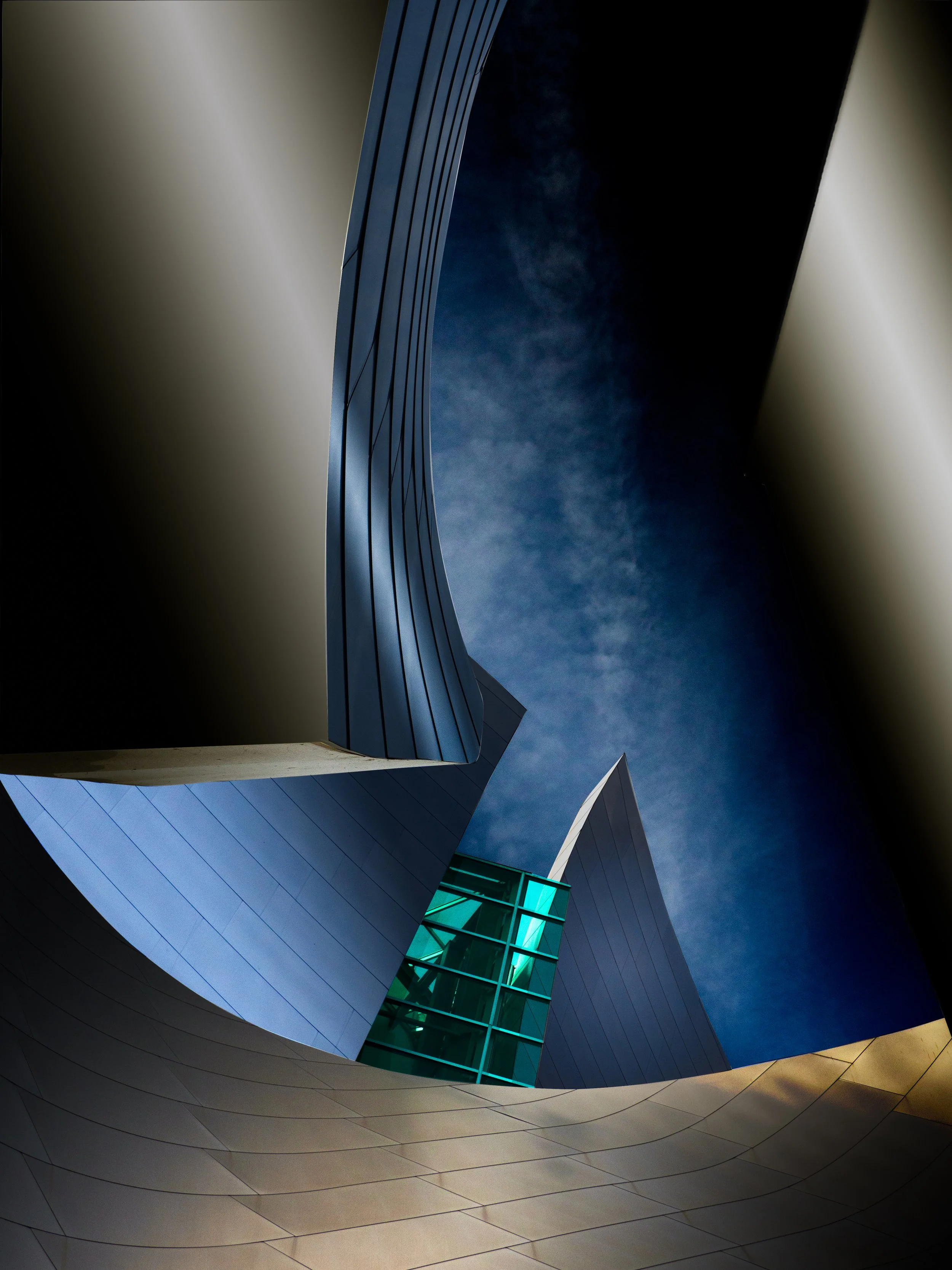 Upward view of a futuristic angular metal building with curved panels, geometric towers, and turquoise glass against a dark blue sky