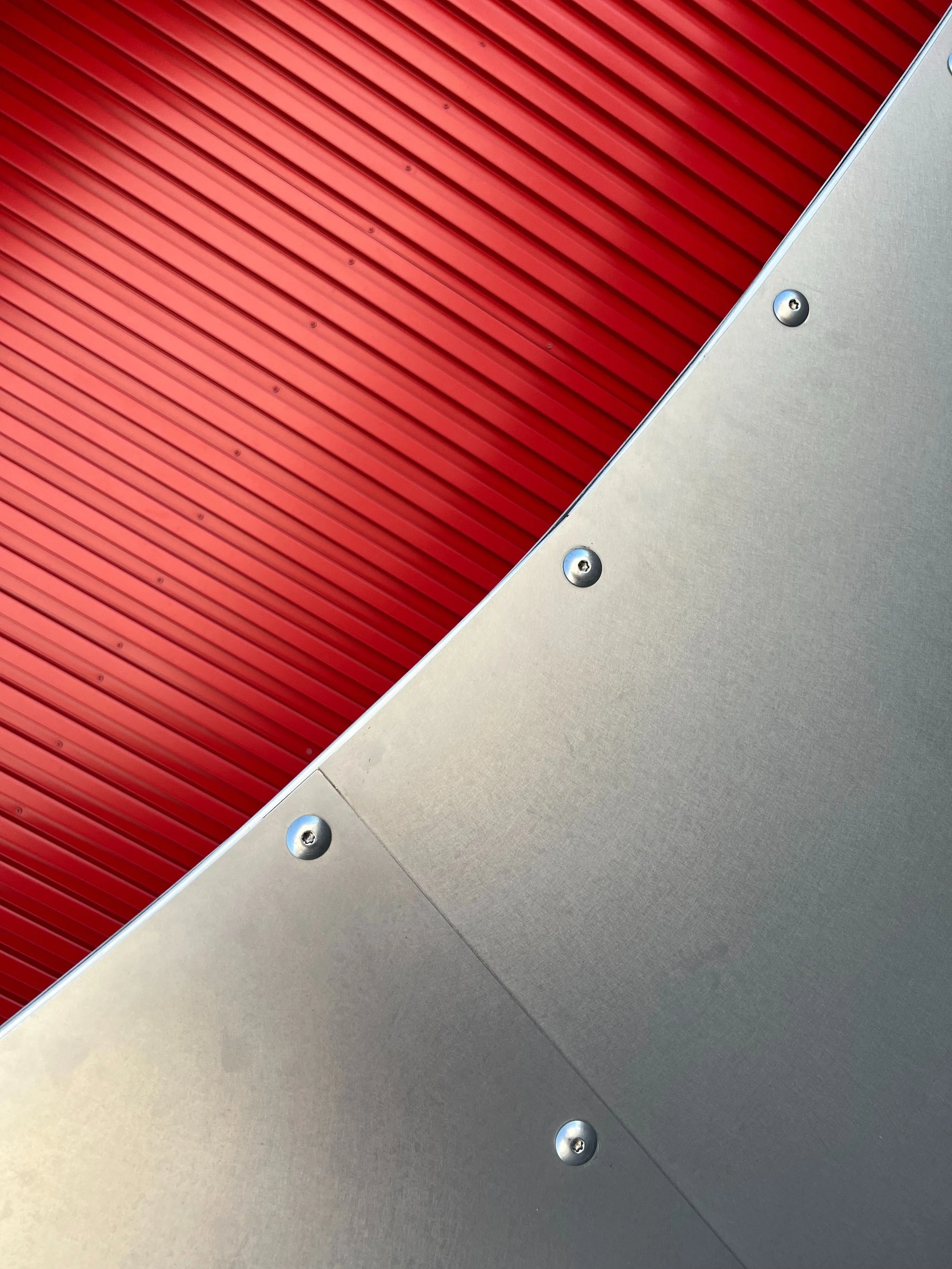 Close-up of red corrugated metal roofing panels with exposed fasteners beside gray metal flashing.
