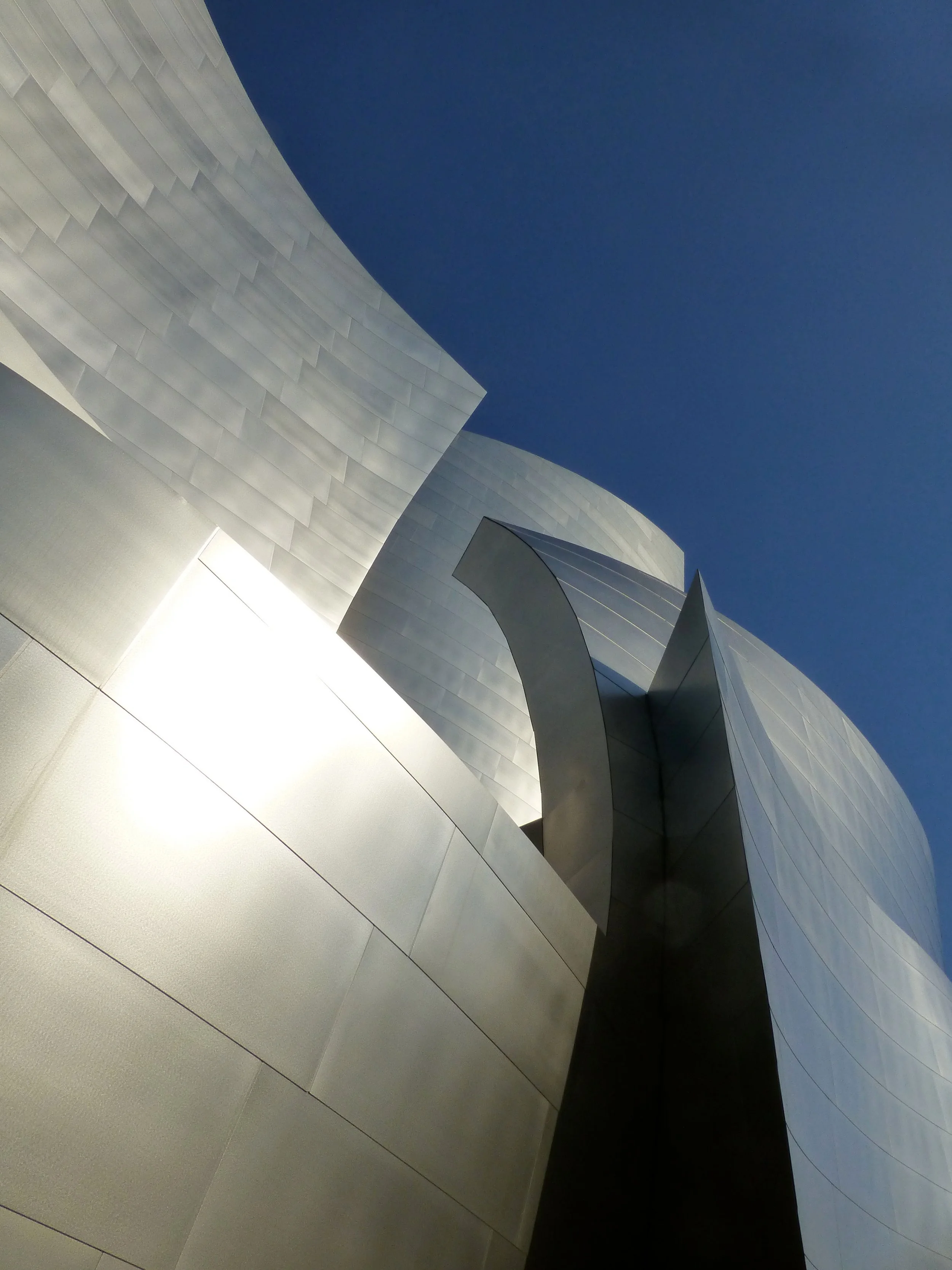 Upward view of a modern white geometric building with angular panels against a deep blue sky