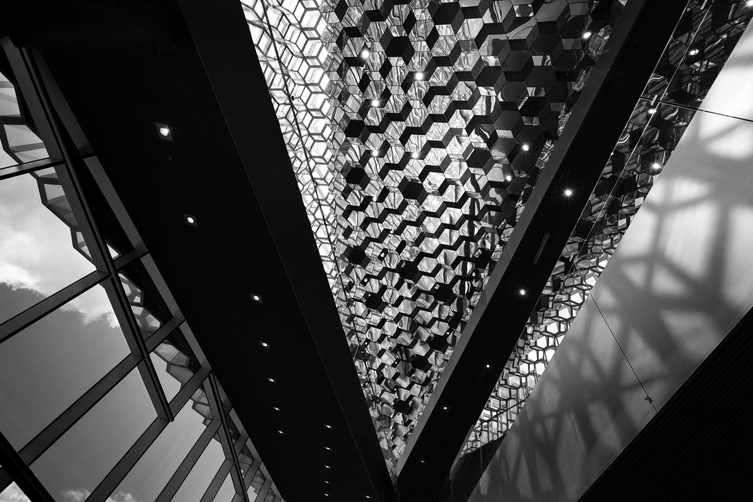 Black-and-white upward view of a modern glass ceiling with a geometric honeycomb pattern and structural beams