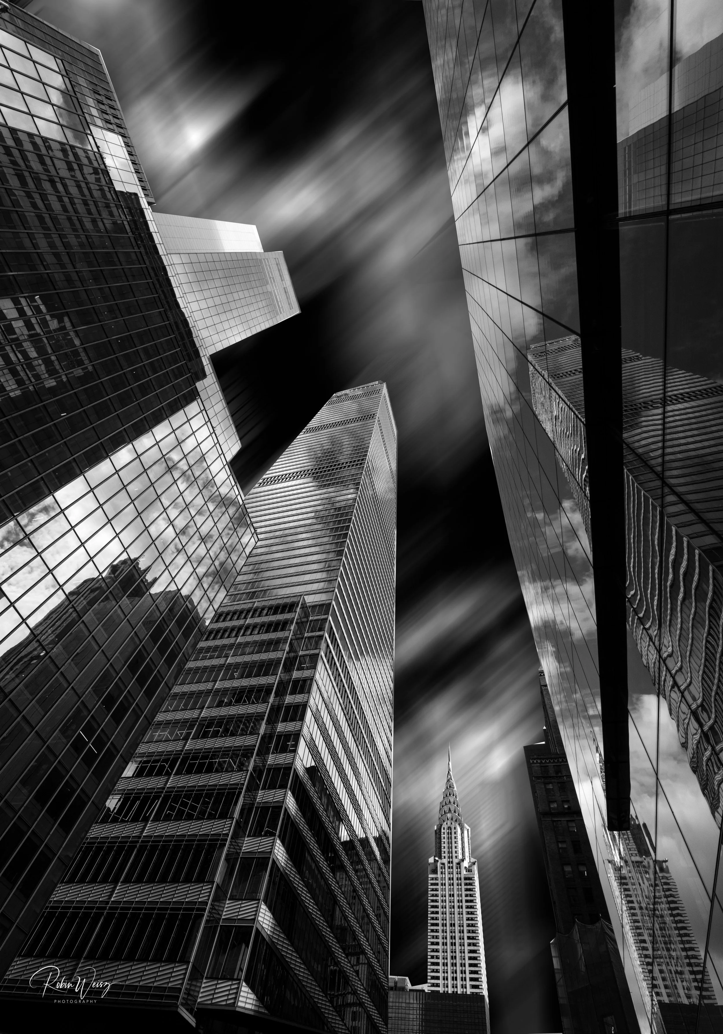 Black-and-white upward view of Manhattan skyscrapers, including the Chrysler Building, with dramatic streaked clouds and reflective glass facades.