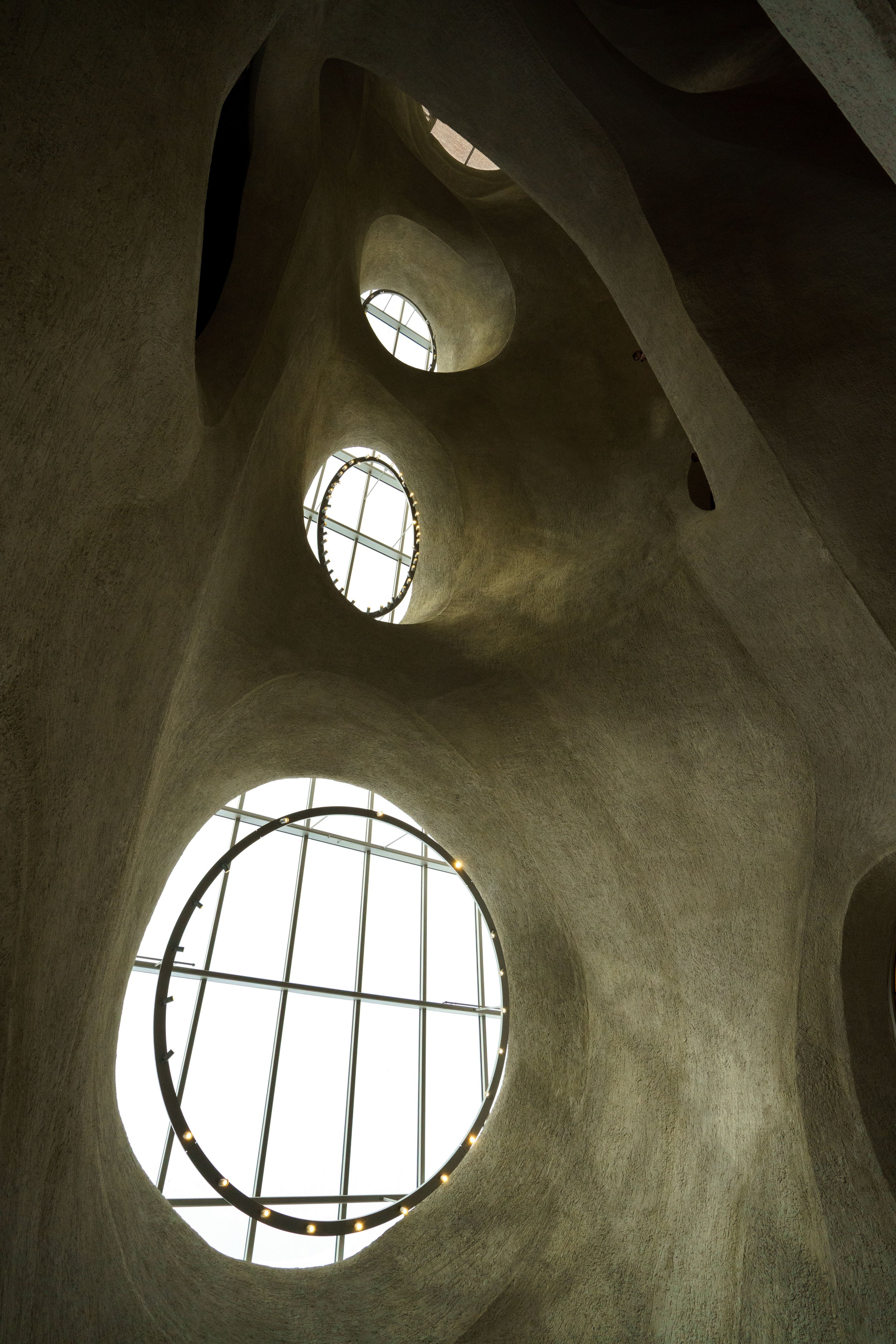 Interior of a sculptural concrete building with curving walls, vaulted arches, and circular skylights.