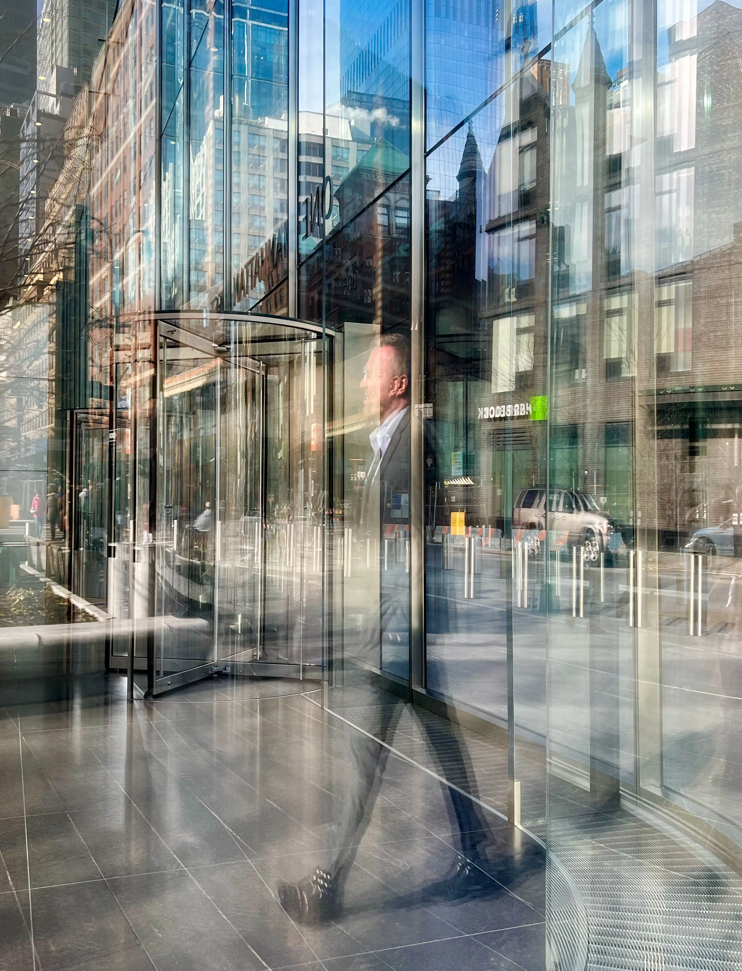 Glass office building entrance reflecting surrounding skyscrapers and historic city buildings