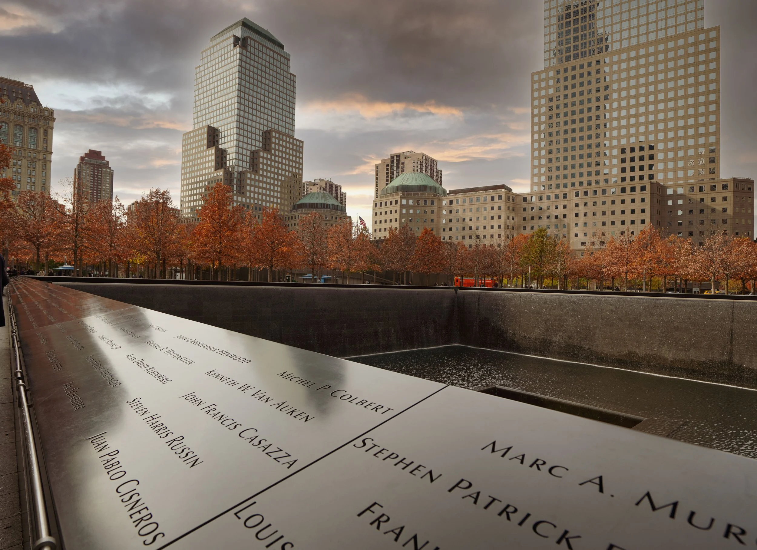 9/11 Memorial reflecting pools and engraved victims’ names with autumn trees and Lower Manhattan skyscrapers in the background