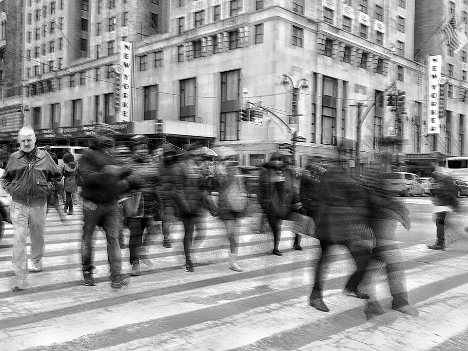 Black-and-white street scene with pedestrians crossing in front of the New Yorker Hotel in New York City.