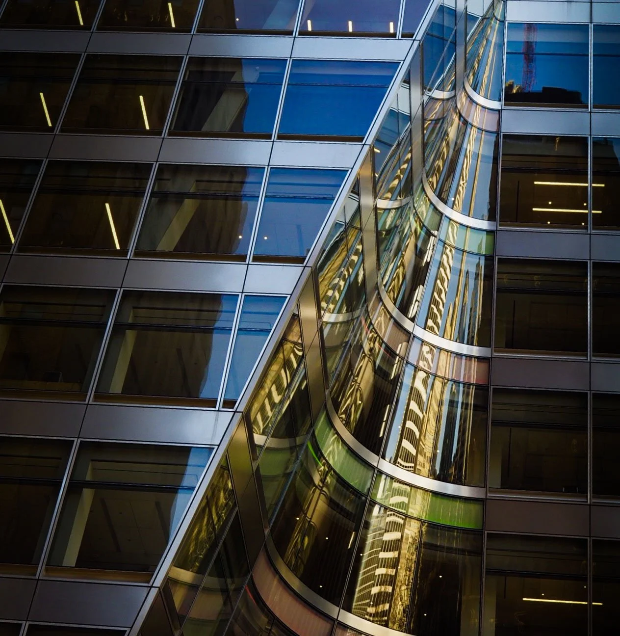 Modern glass office building facade with geometric windows and dramatic reflections