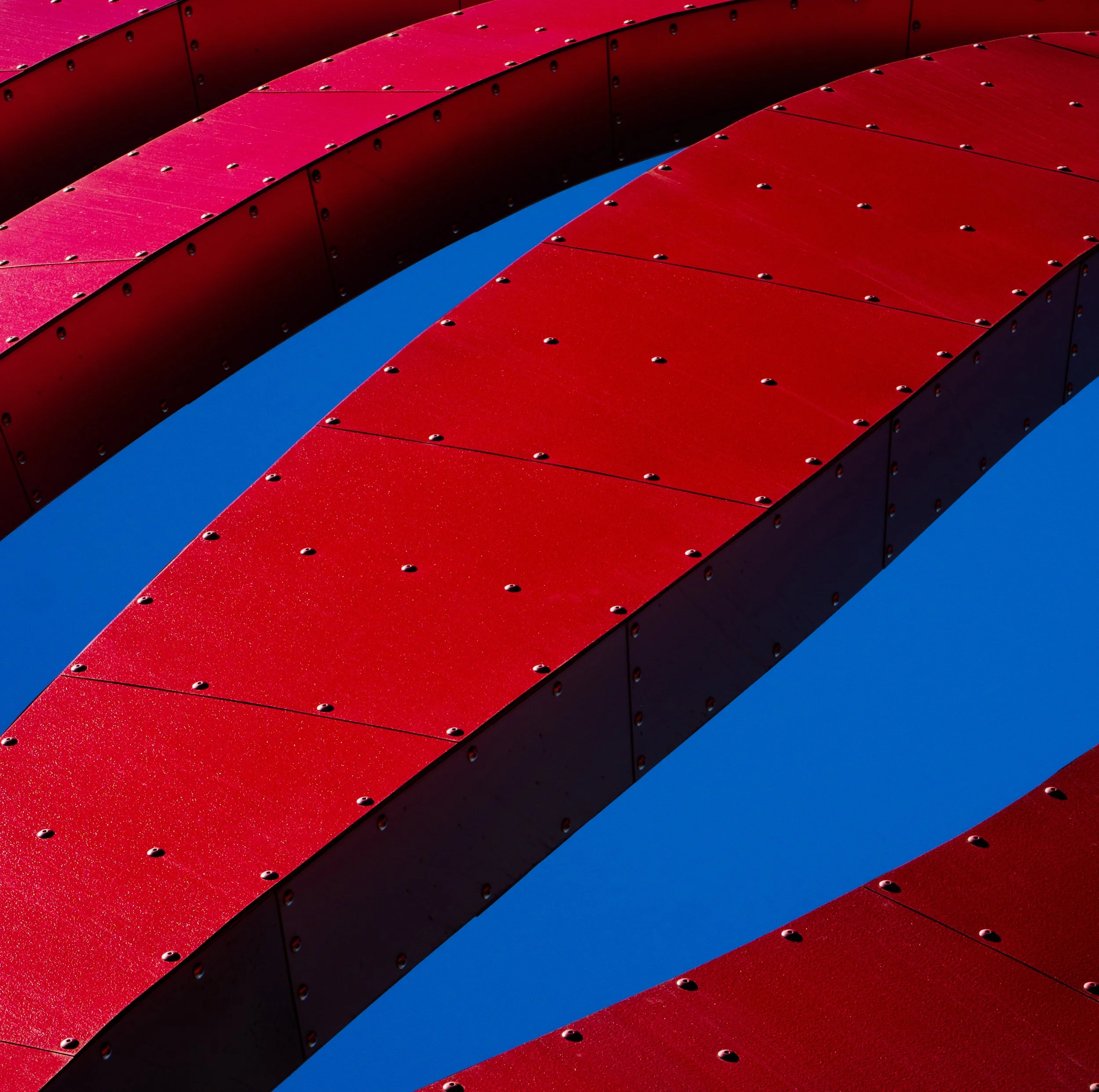 Abstract geometric pattern of red riveted metal panels arranged in parallel rows over a vivid blue background
