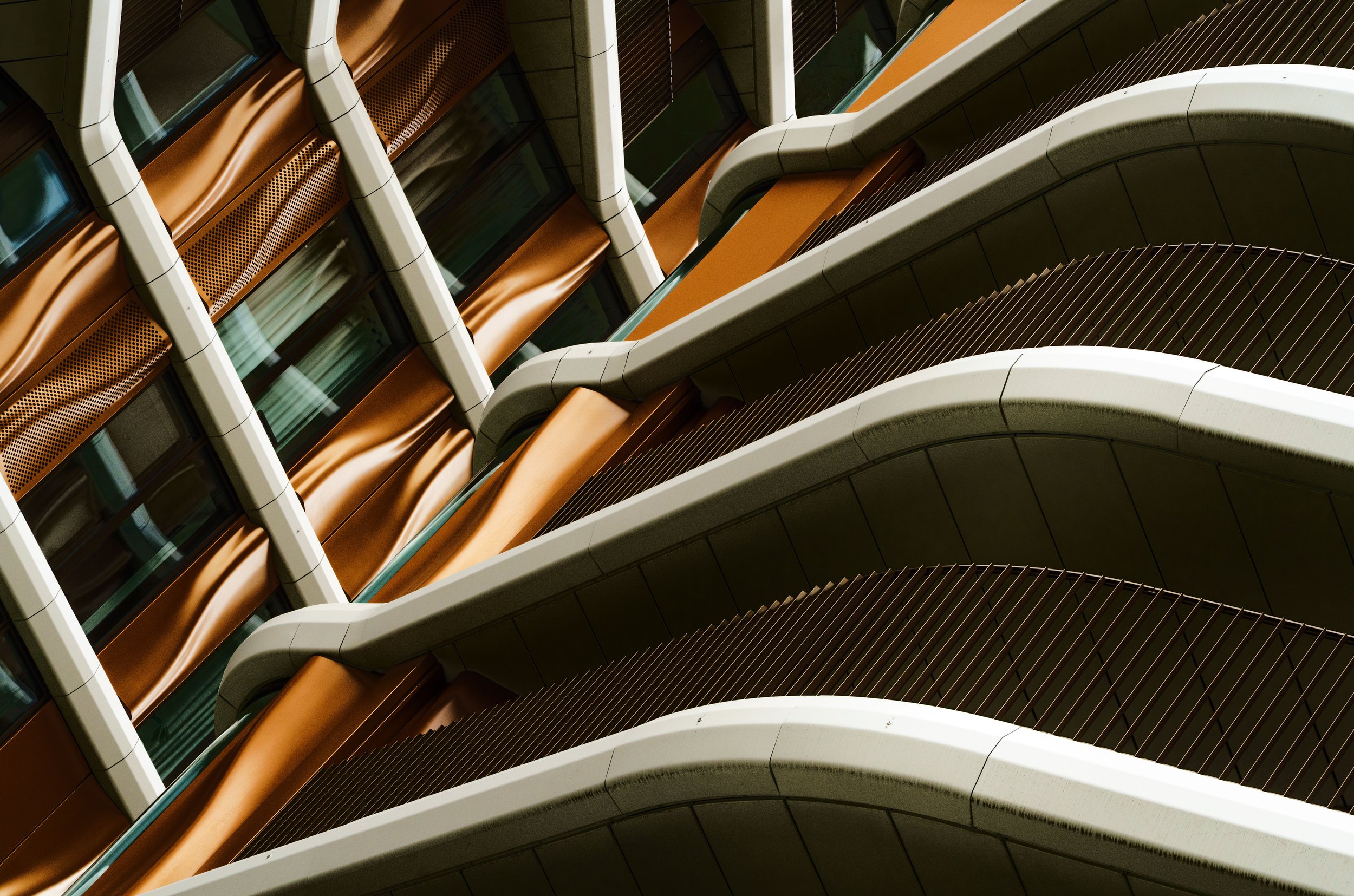 Abstract architectural view of a modern building facade with curved white beams, copper panels, glass windows, and dark vertical slats